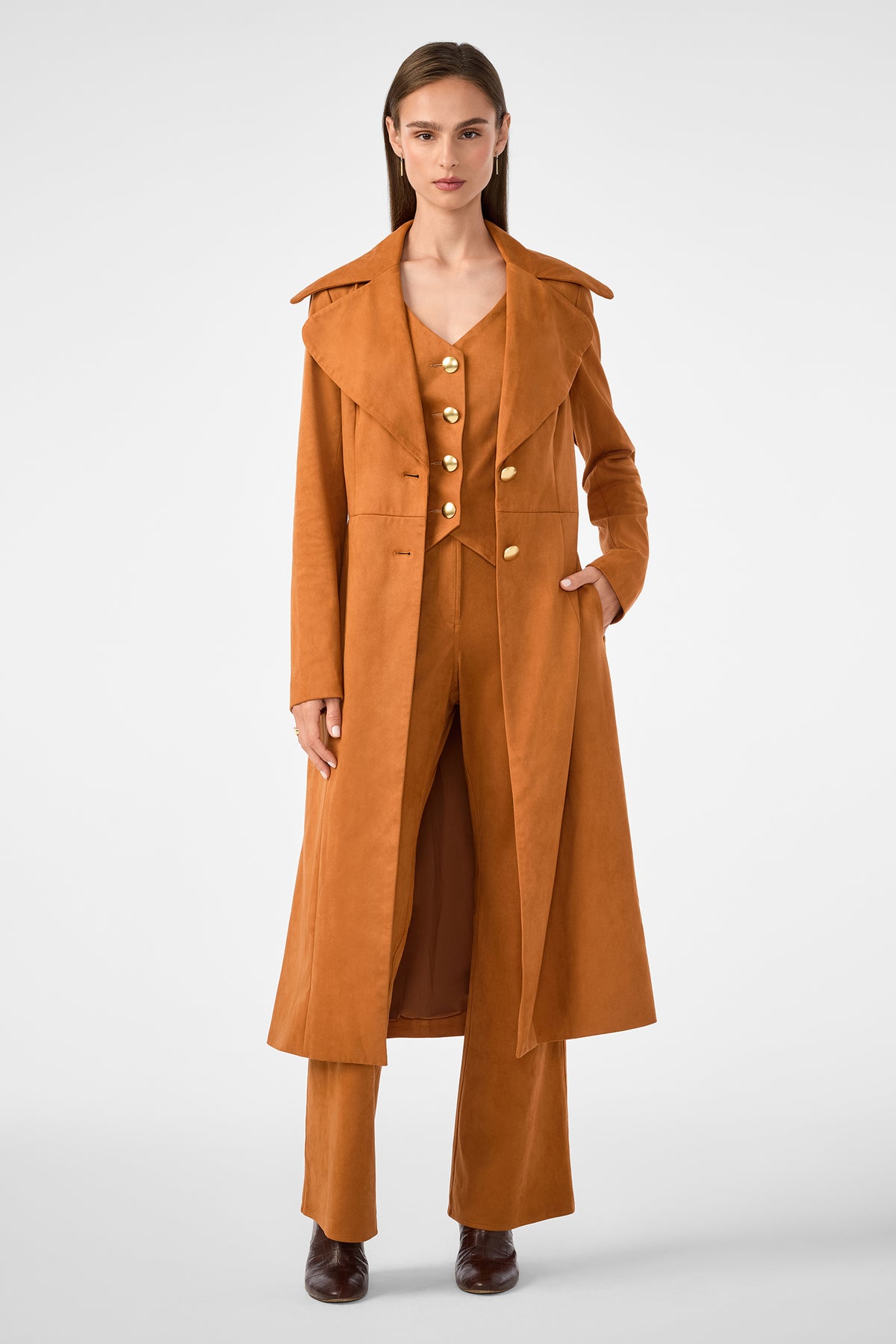 A woman faces forward in a rust suede coat over the Kofi 2 Vest and matching wide-leg pants. She has straight brown hair, brown shoes, and stands against a plain light background.
