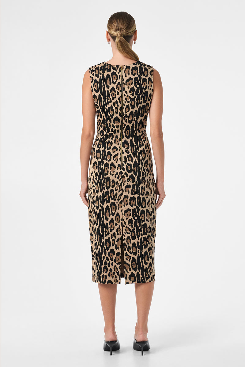 A woman with straight blonde hair in a low ponytail models the Dame Dress—a sleeveless, knee-length leopard print dress paired with black heels—standing with her back to the camera against a plain white background.