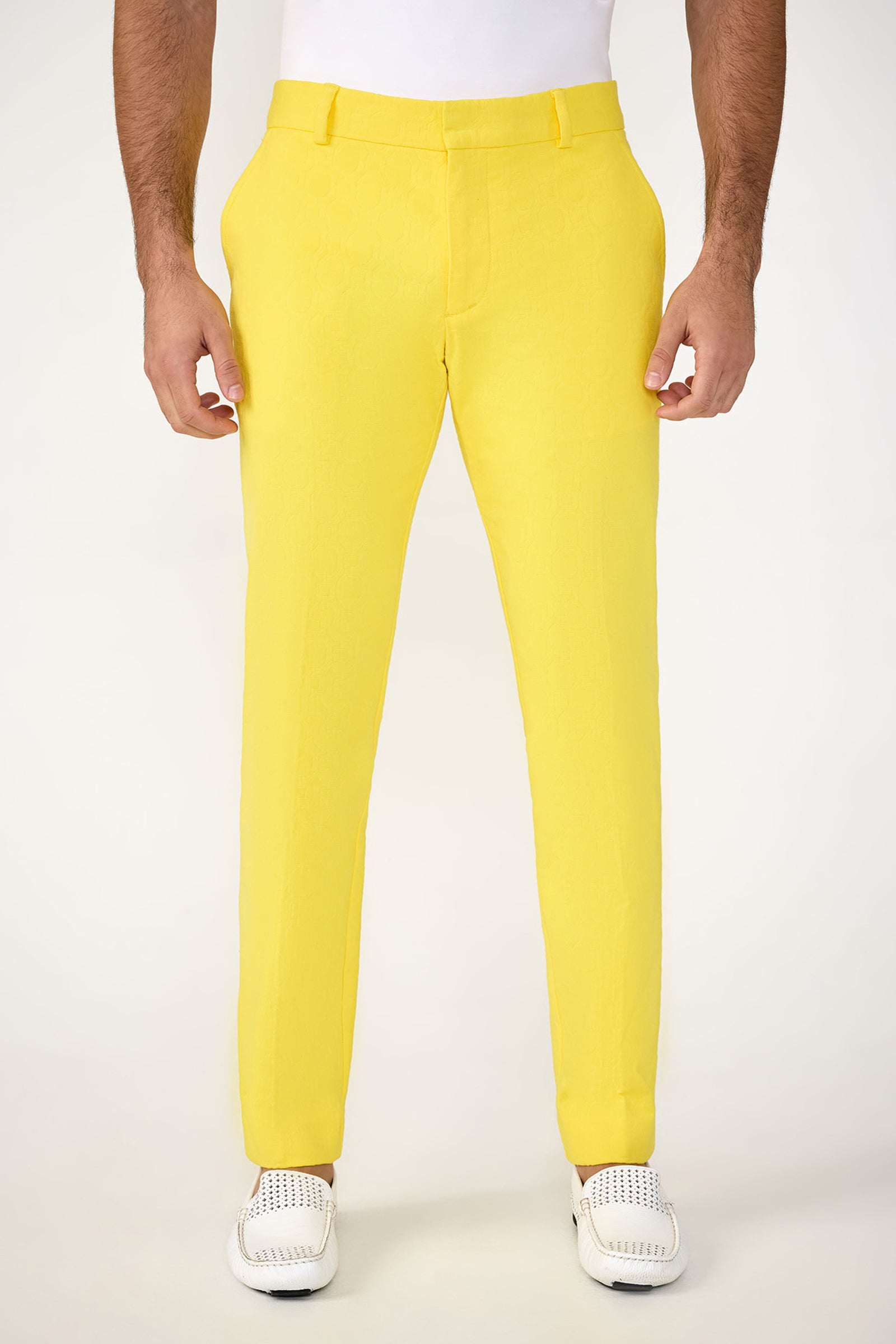 A person wearing Clyde Slim Trouser - Stretch Herringbone in Lavandou Lemon and a tucked-in white shirt with white perforated slip-on shoes, standing against a plain light background. The image is cropped at the shoulders.