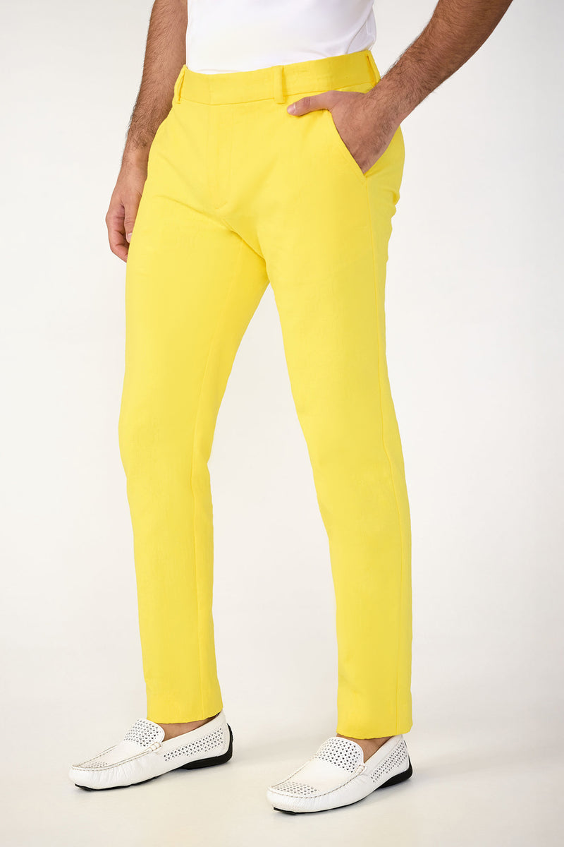 A man stands against a light background wearing the Clyde Slim Trouser - Stretch Herringbone in bright yellow, paired with a white shirt and perforated white slip-on shoes, with one hand tucked in his pocket.