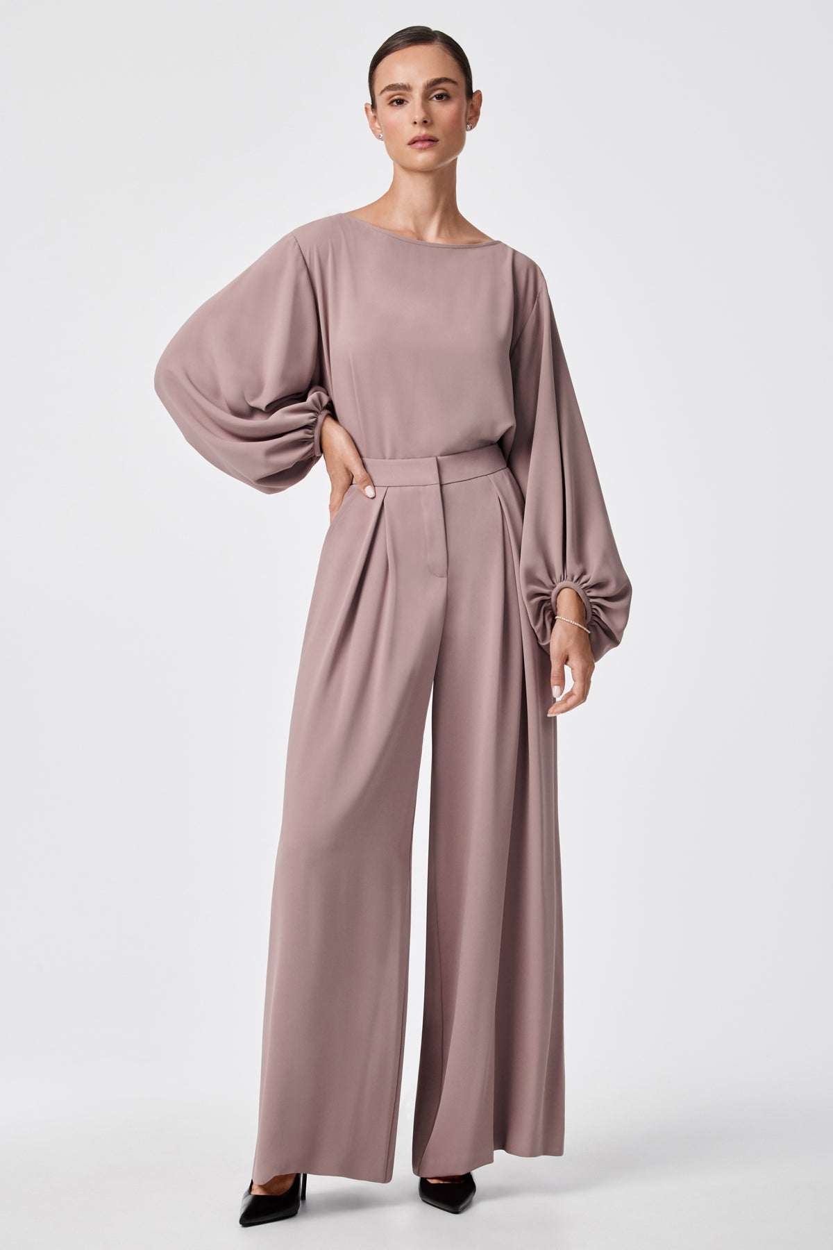 A woman wears Saige Wide-Leg Short Pants in mauve with a matching billowy long-sleeve blouse and black pointed-toe heels, standing against a plain white background.