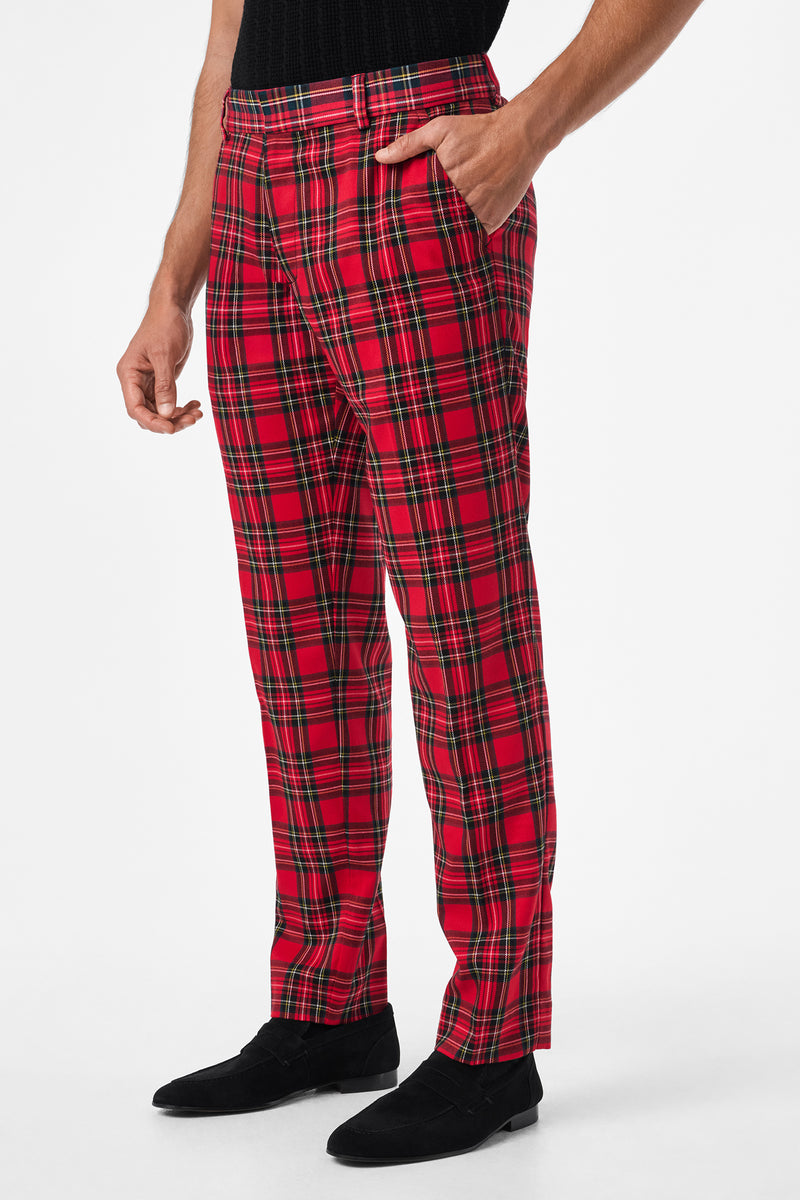 A person wearing Clyde Slim Trouser - Can-Can Check, featuring red plaid with black, yellow, and green lines, paired with a black top and black shoes, stands with one hand in their pocket against a white background.