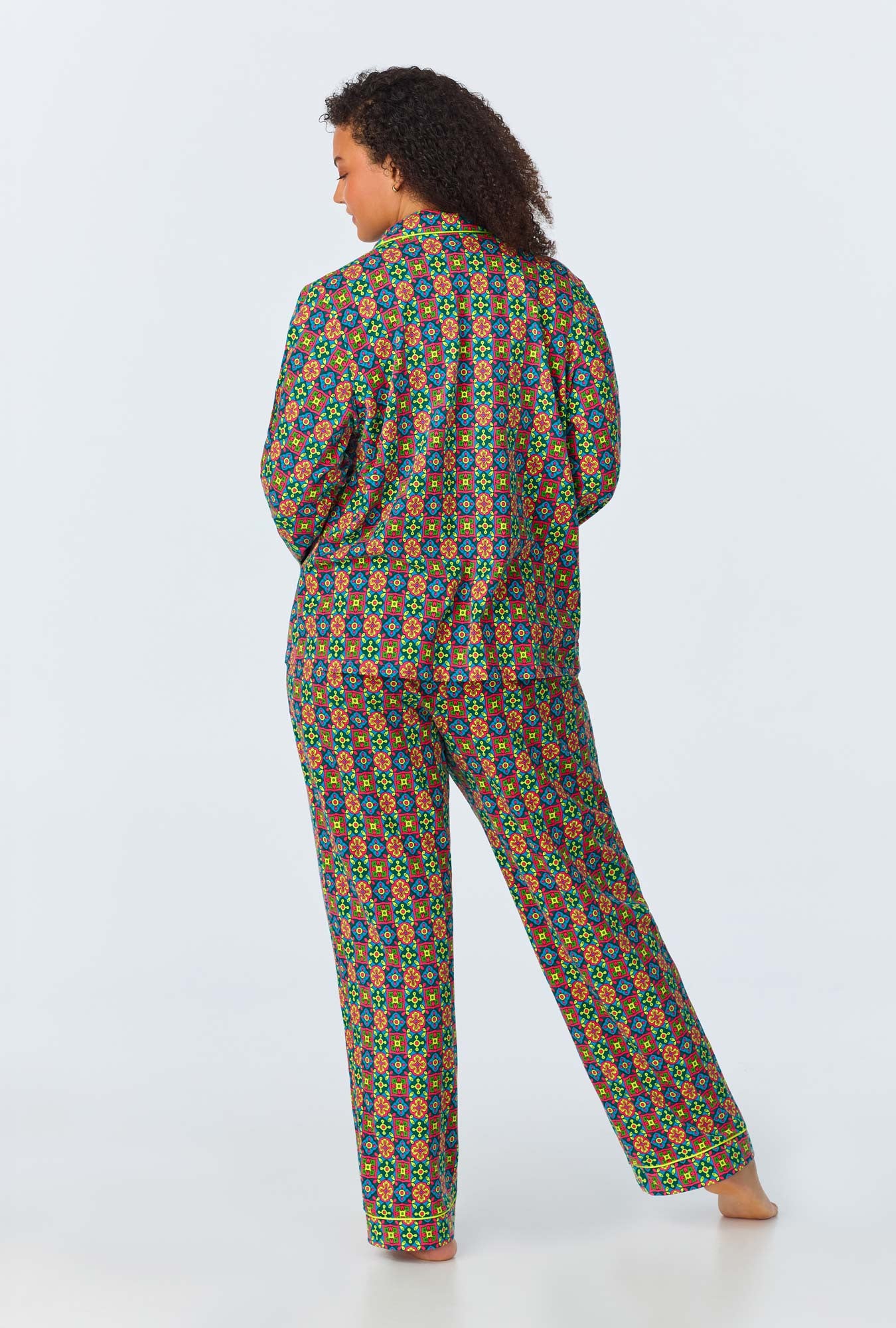 A person stands barefoot with their back to the camera, wearing the Pretty Tiles Womens Long Sleeve Long Pant Jersey PJ Set, which features a colorful geometric pattern of small, multicolored shapes on a dark background.
