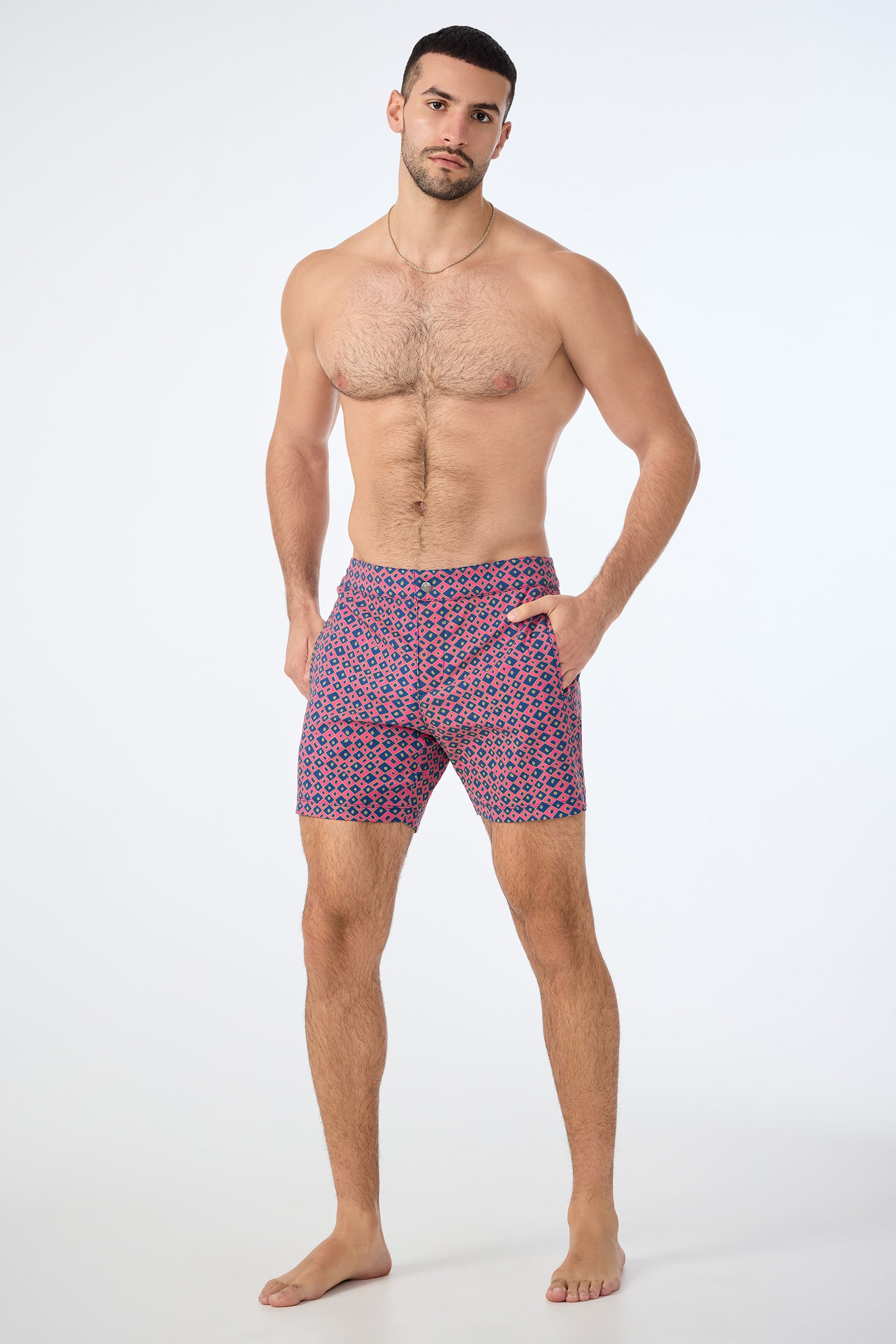 A barefoot man with short dark hair stands confidently against a plain white background, wearing the Honolulu Board Short - Himari Herringbone. His hands are in his pockets as he looks straight at the camera.