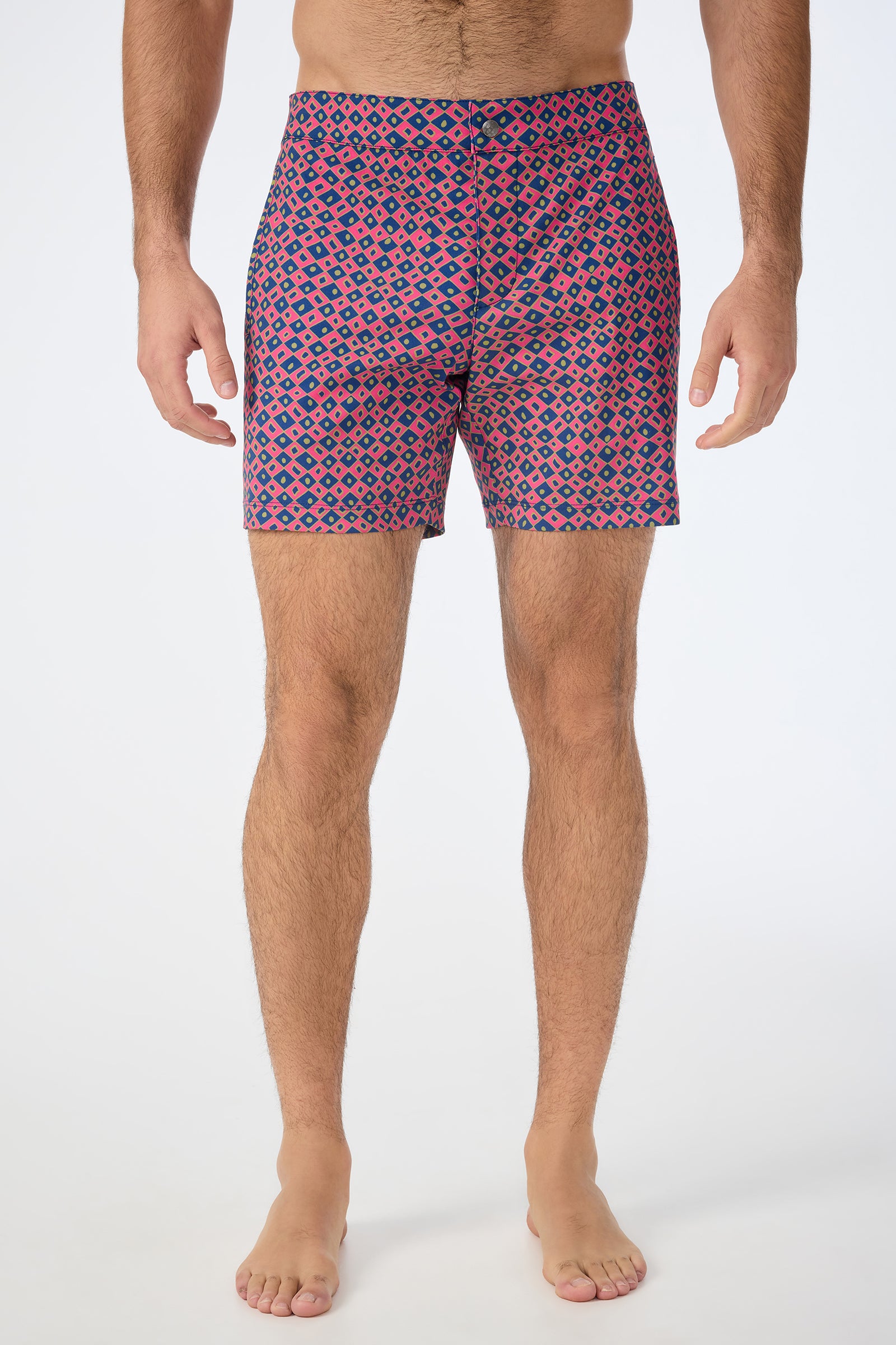 A man stands barefoot wearing Honolulu Board Short - Himari Herringbone, featuring a pink, blue, and black geometric design. His upper body is not visible; the background is plain white.