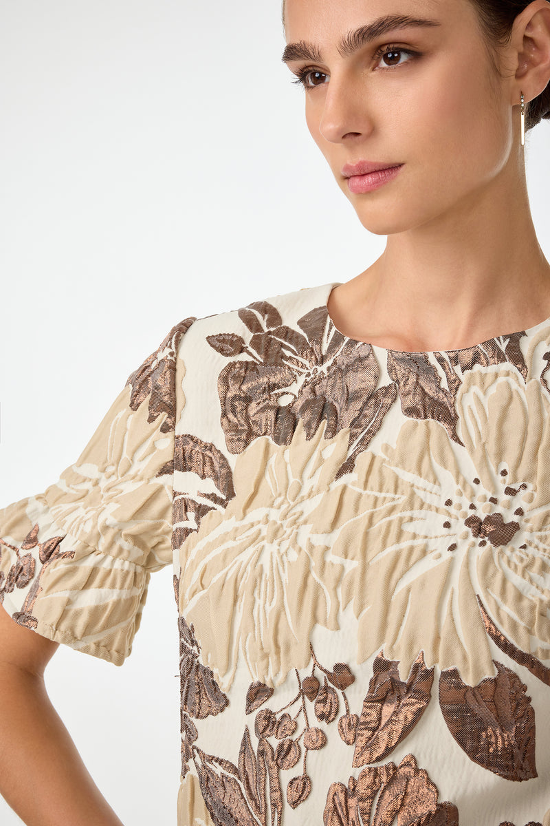 A woman wearing the Darling Flounce Sleeve Dress, featuring a cream color with large brown and beige floral patterns, stands against a plain background, gazing slightly to the side with a neutral expression.