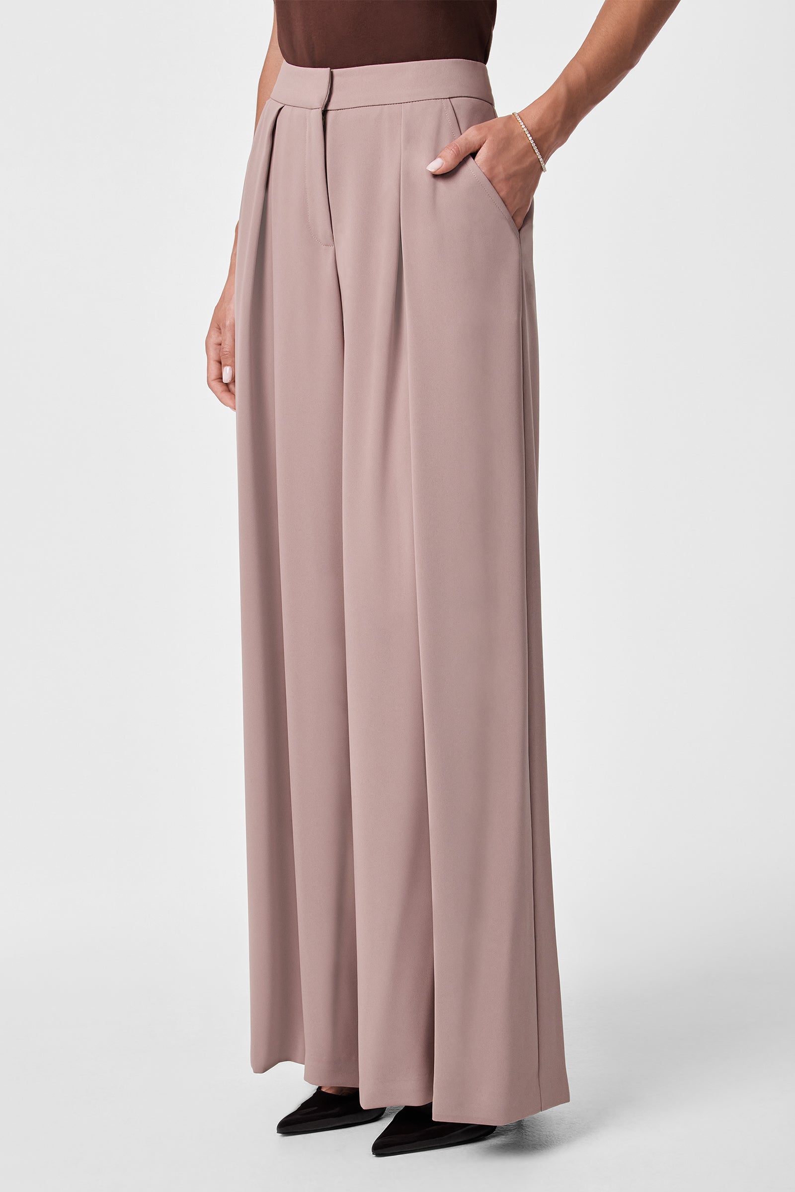 Someone stands on a plain white background wearing Saige Wide-Leg Short Pants in light mauve, featuring a high waist, wide legs, and side pockets, paired with black pointed-toe shoes. Only the lower body is fully visible.