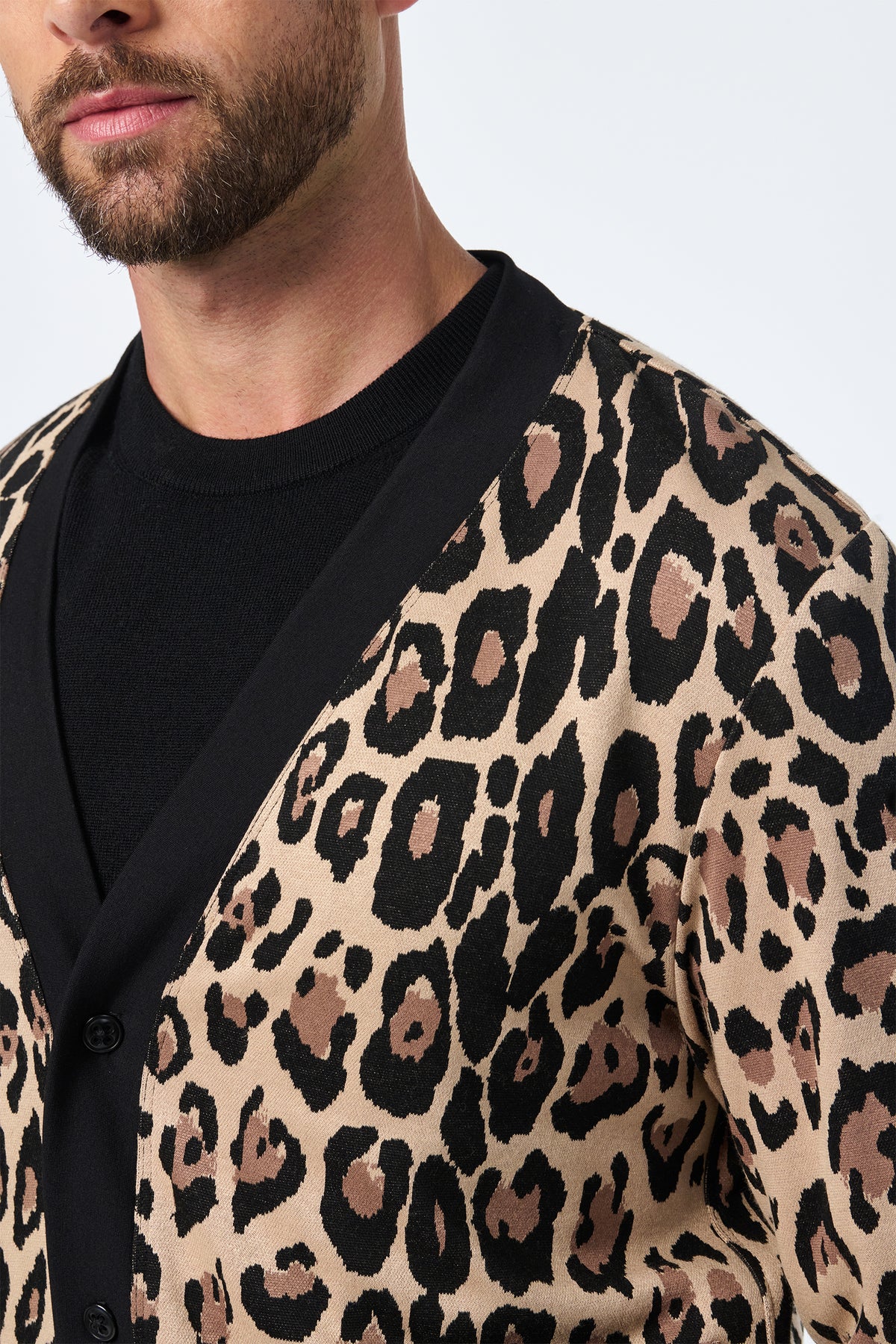 A man with a trimmed beard wears the Darryl Knit Cardigan, featuring a bold black and brown leopard print over beige, paired with a black shirt. The photo partially shows his face and upper body.
