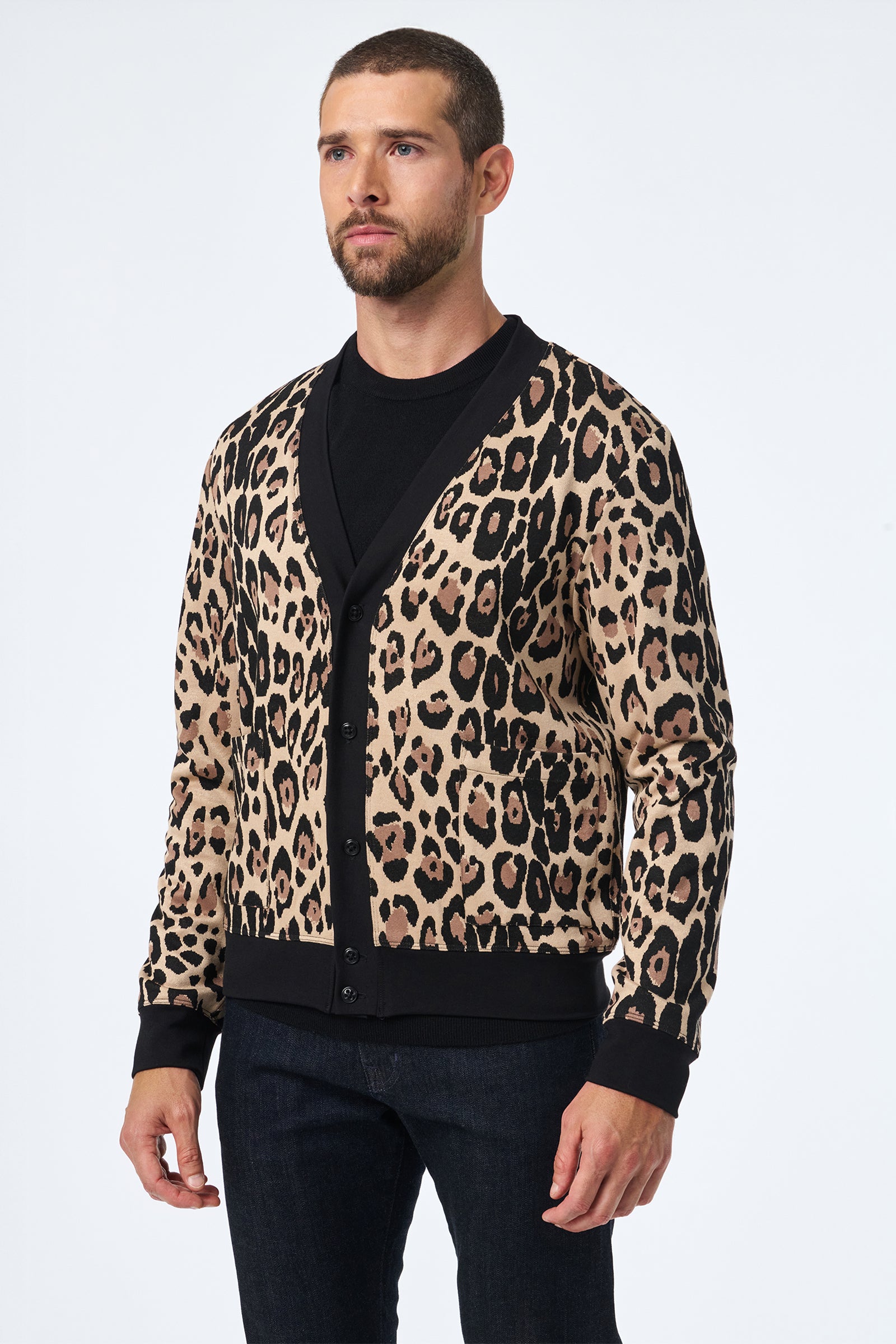 A man faces forward wearing the Darryl Knit Cardigan, featuring a tan and black leopard print, layered over a black shirt and dark jeans against a plain white background.