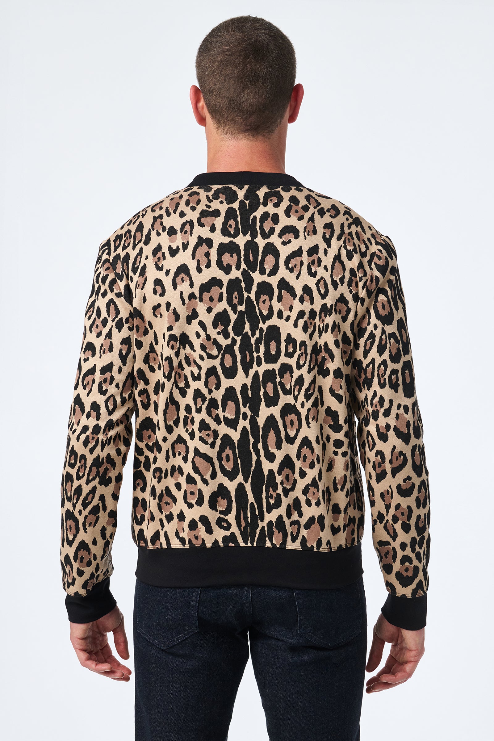 A man with short hair, seen from the back, wears the Darryl Knit Cardigan—a long-sleeve leopard print cardigan featuring black trim at the cuffs and hem—while standing against a plain white background.