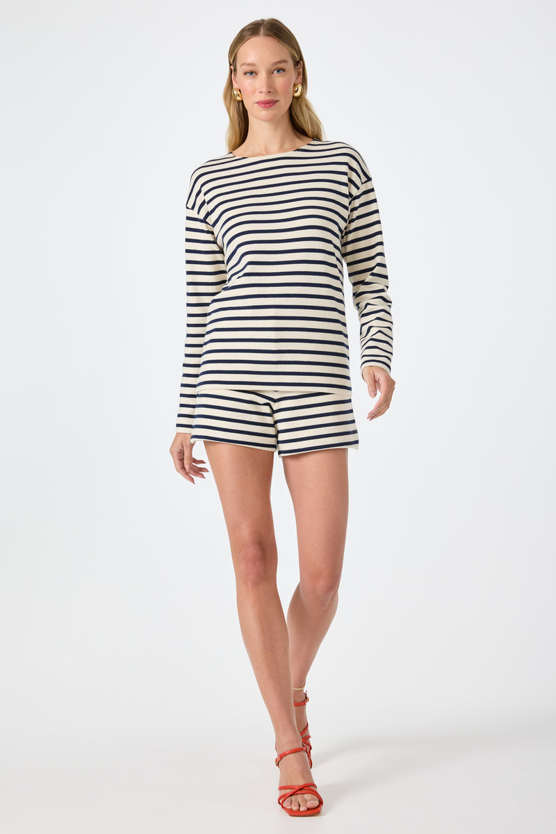 A woman stands against a plain white background wearing the Corbin 2 Shorts in Noh Nightfall Stripe with a matching long-sleeve black and white striped top and red strappy sandals.