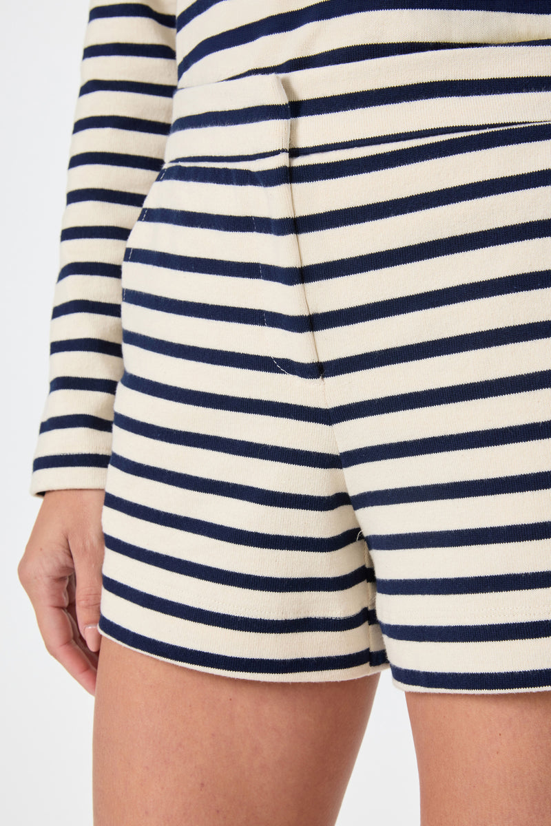 Close-up of a person wearing the Corbin 2 Shorts in Noh Nightfall Stripe with a matching long-sleeve top in cream and navy stripes. Their left hand is relaxed by their side.