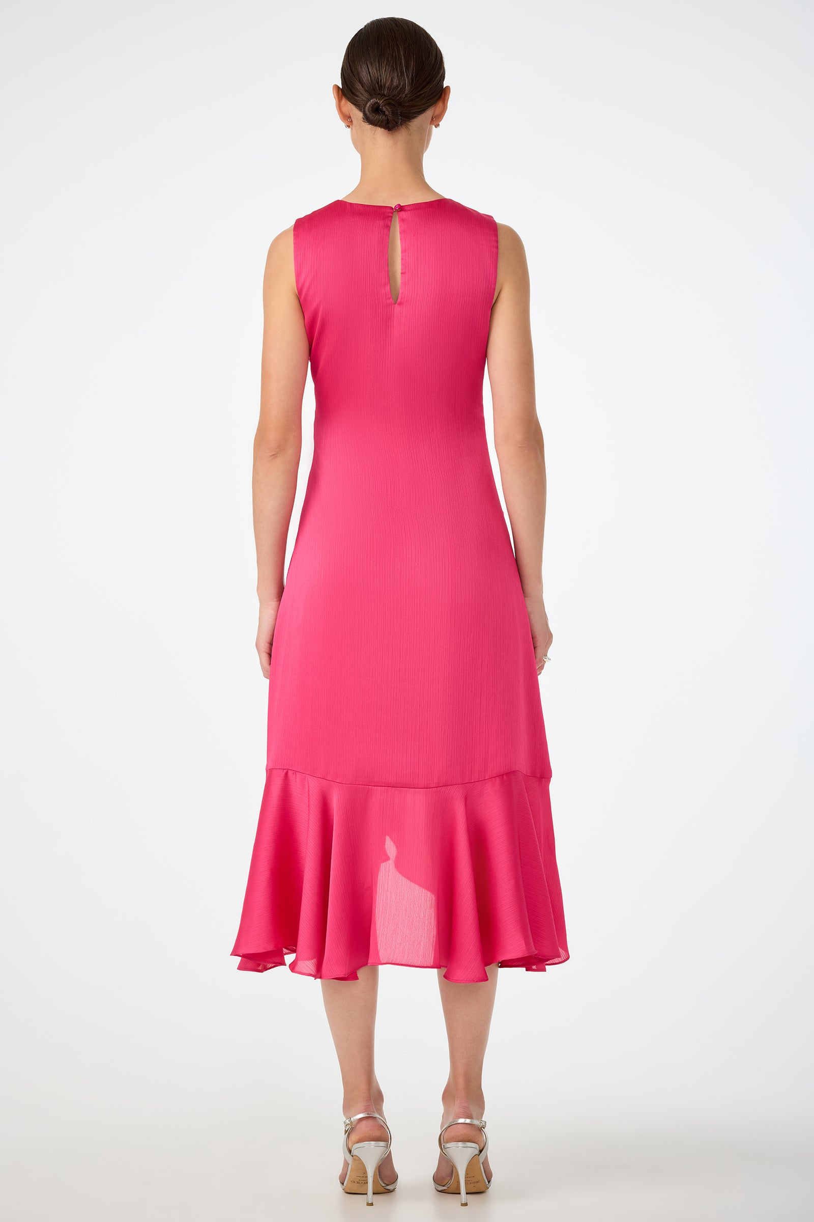 A woman faces away, wearing the Amara 2 Sleeveless Ruffle Dress—a bright pink, midi-length style with a ruffled hem and keyhole back—paired with silver high-heeled sandals.