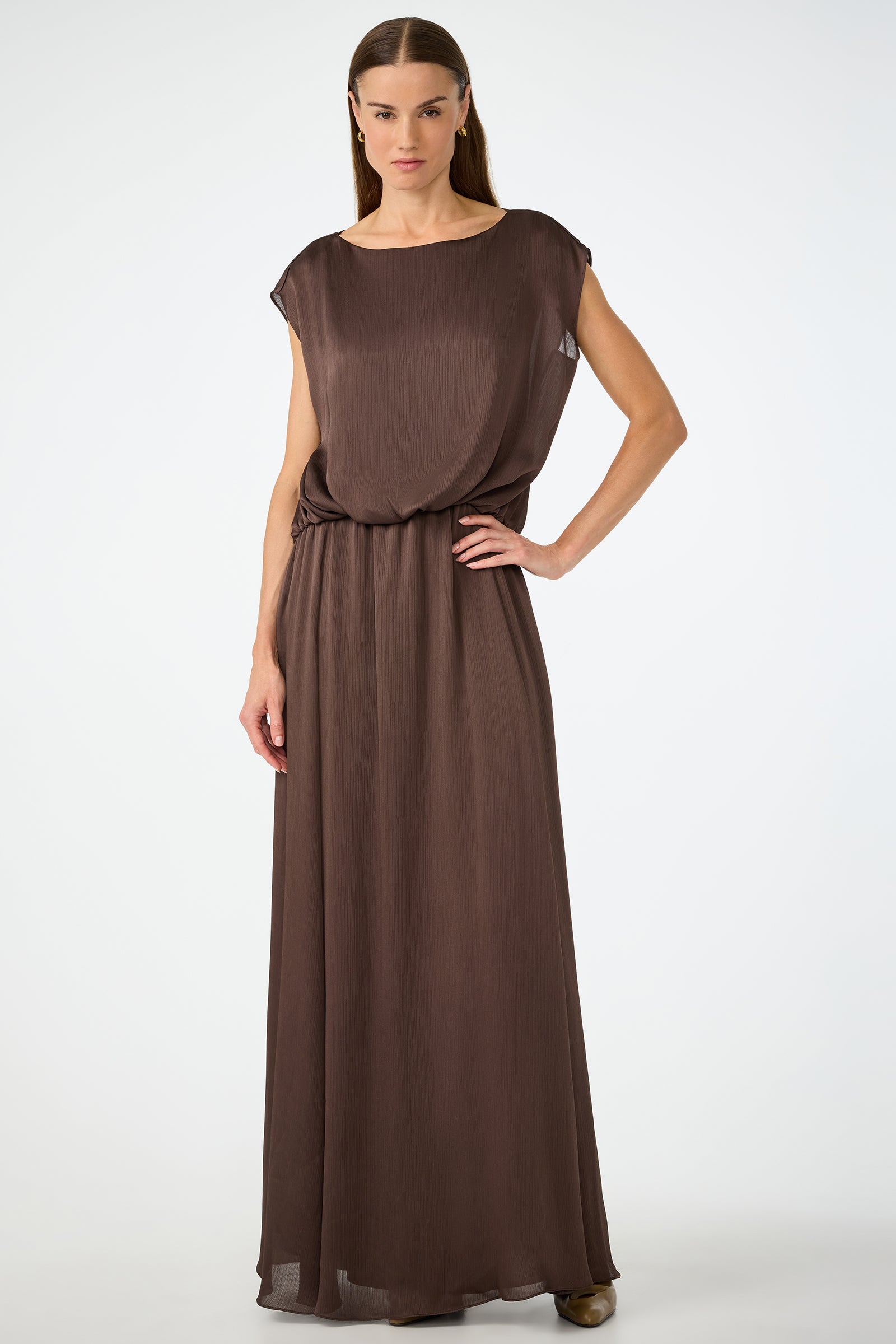 A woman poses confidently against a plain background, wearing the Vantage 2 Maxi Dress in Walnut—a sleeveless, loose-fitting design with a cinched waist. She has straight hair and rests one hand on her hip.