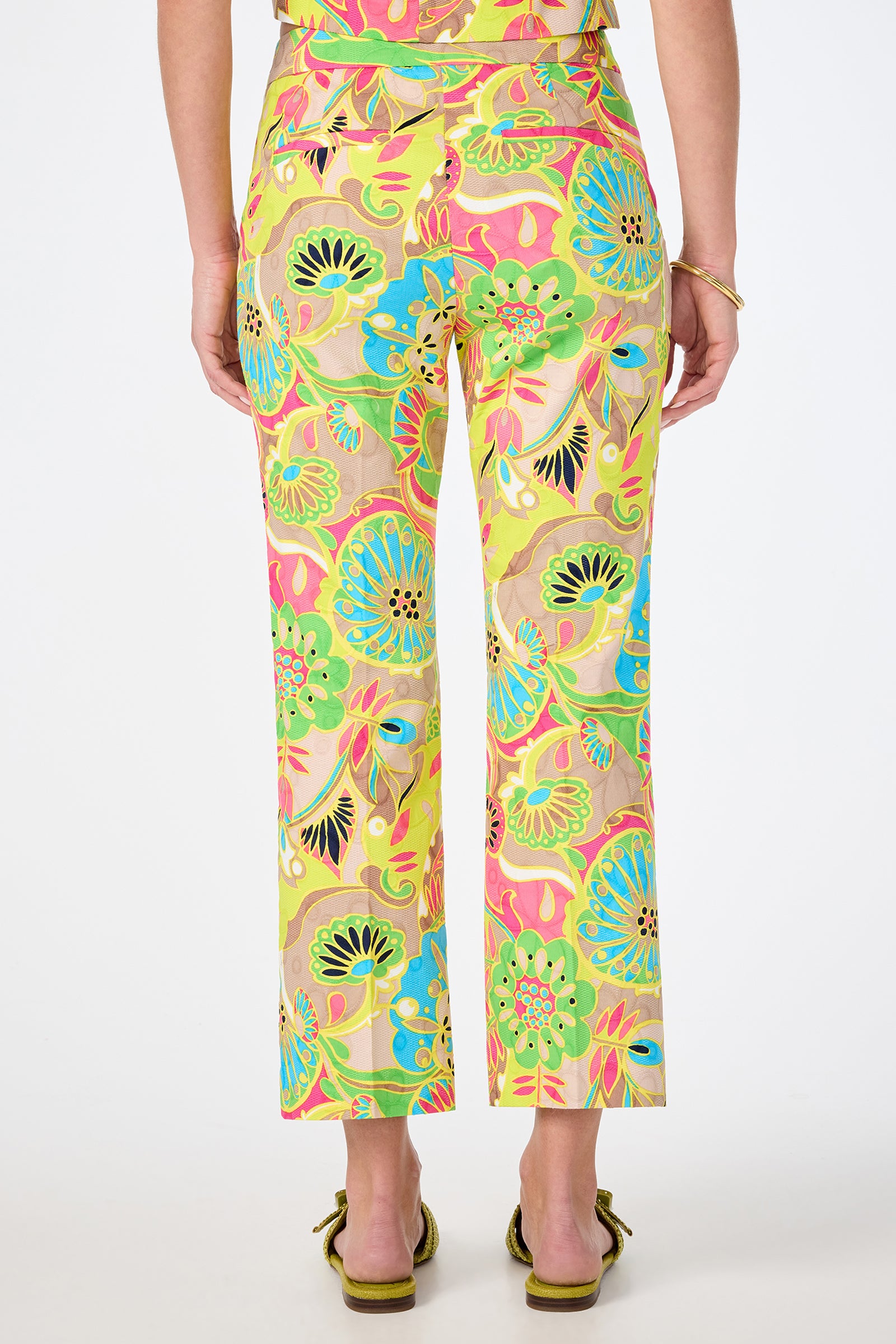 A person is shown from the back wearing the Lulu Cropped Pant - Venus, featuring a high-waisted, straight-leg fit and a vibrant multicolored floral pattern, paired with a matching top and heels.