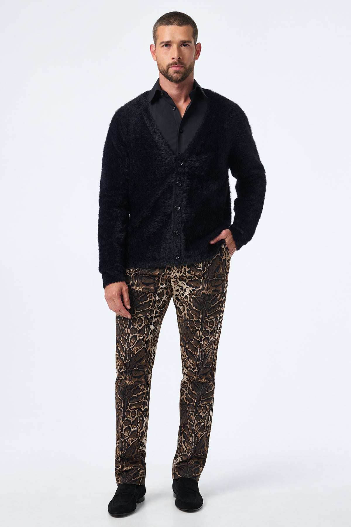 A man faces forward against a plain white background, wearing the Scott Fuzzy Cardigan in black, a black dress shirt, brown leopard-print pants, and black shoes.