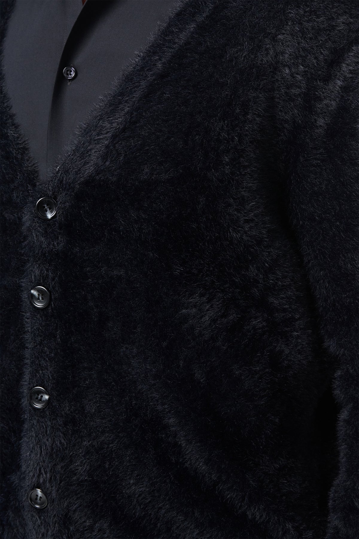 Close-up of a person wearing the Scott Fuzzy Cardigan in black over a black collared shirt. The cardigan has a soft, plush texture and features four visible buttons.