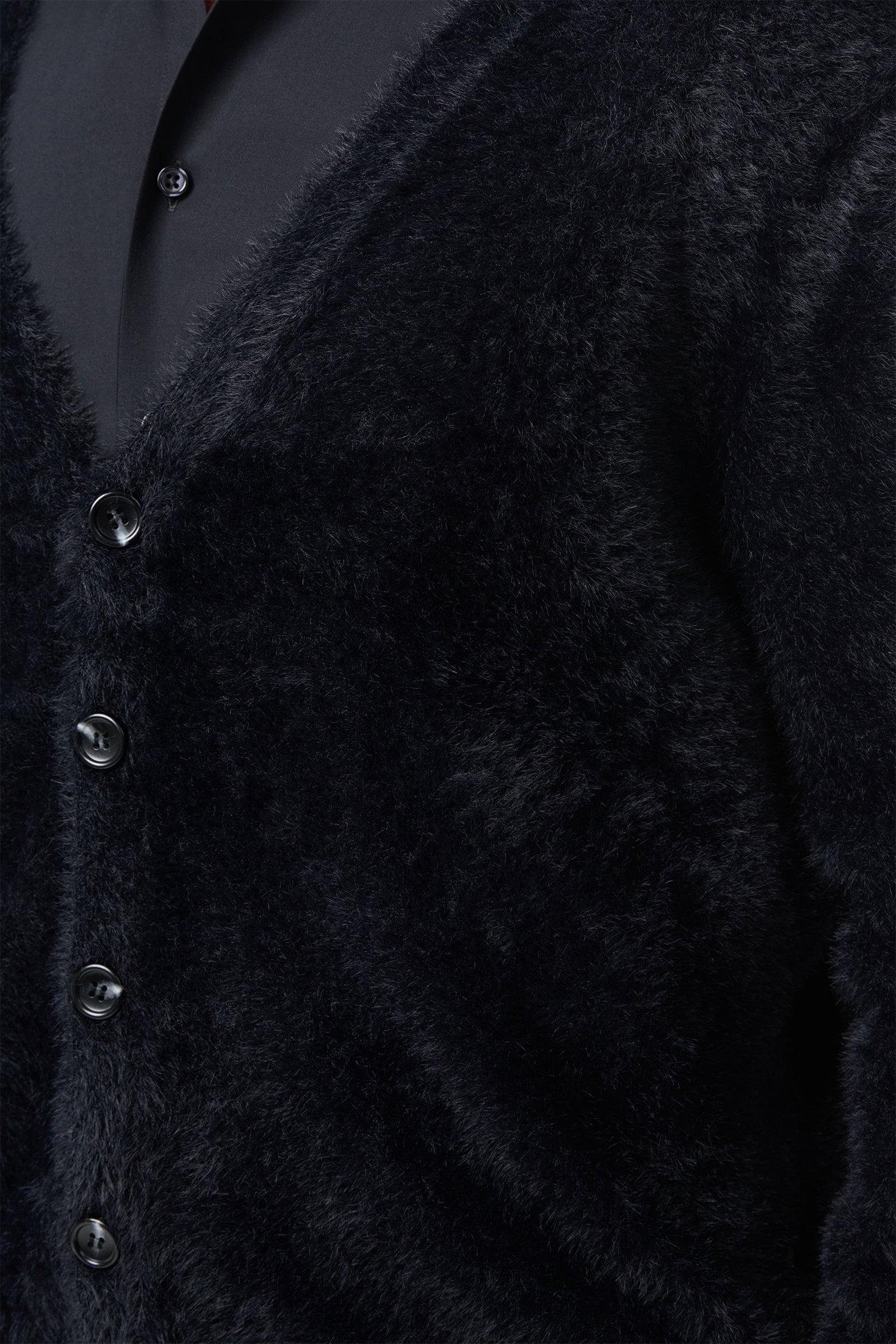 Close-up of a person wearing the Scott Fuzzy Cardigan in black over a black collared shirt. The cardigan has a soft, plush texture and features four visible buttons.