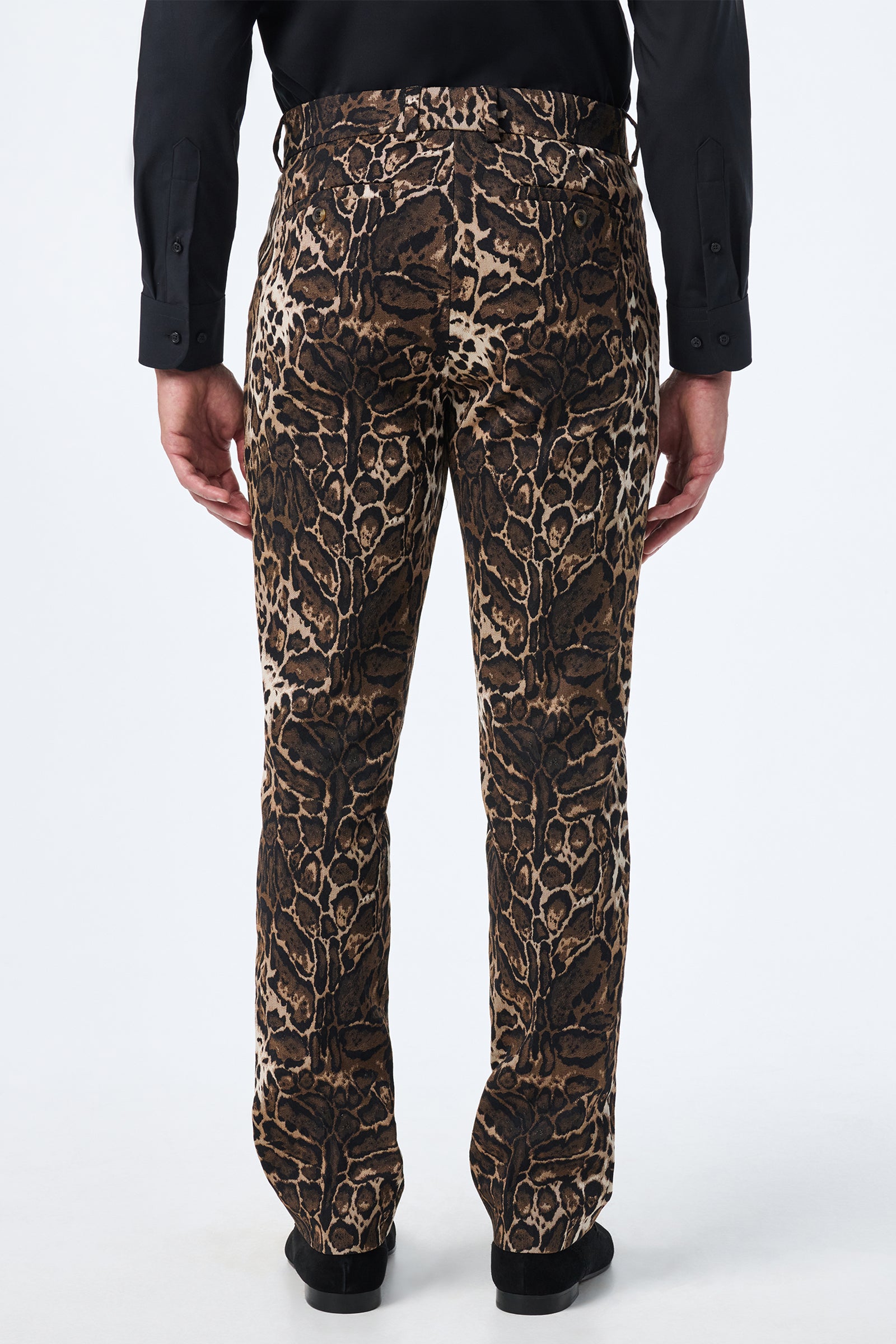 Facing away, the individual wears Clyde Slim Trouser - Lompoul Leopard, featuring brown and black animal print, paired with a black long-sleeve shirt and arms relaxed at their sides.