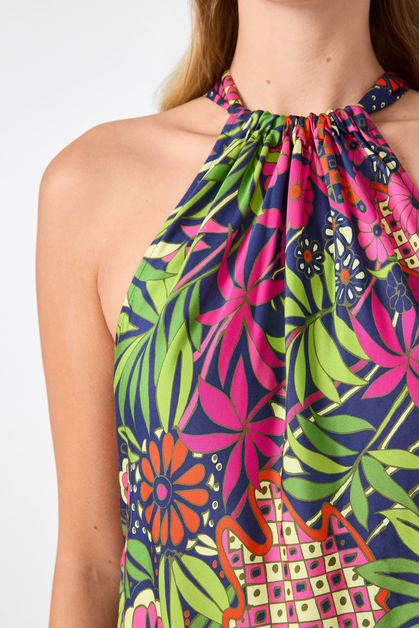 A person wears the Lavani 2 Halter Top - Fumi Floral, featuring a sleeveless halter-neck design with bold green, pink, orange, and navy floral and geometric prints. Only their upper chest, neck, and part of the face are visible.