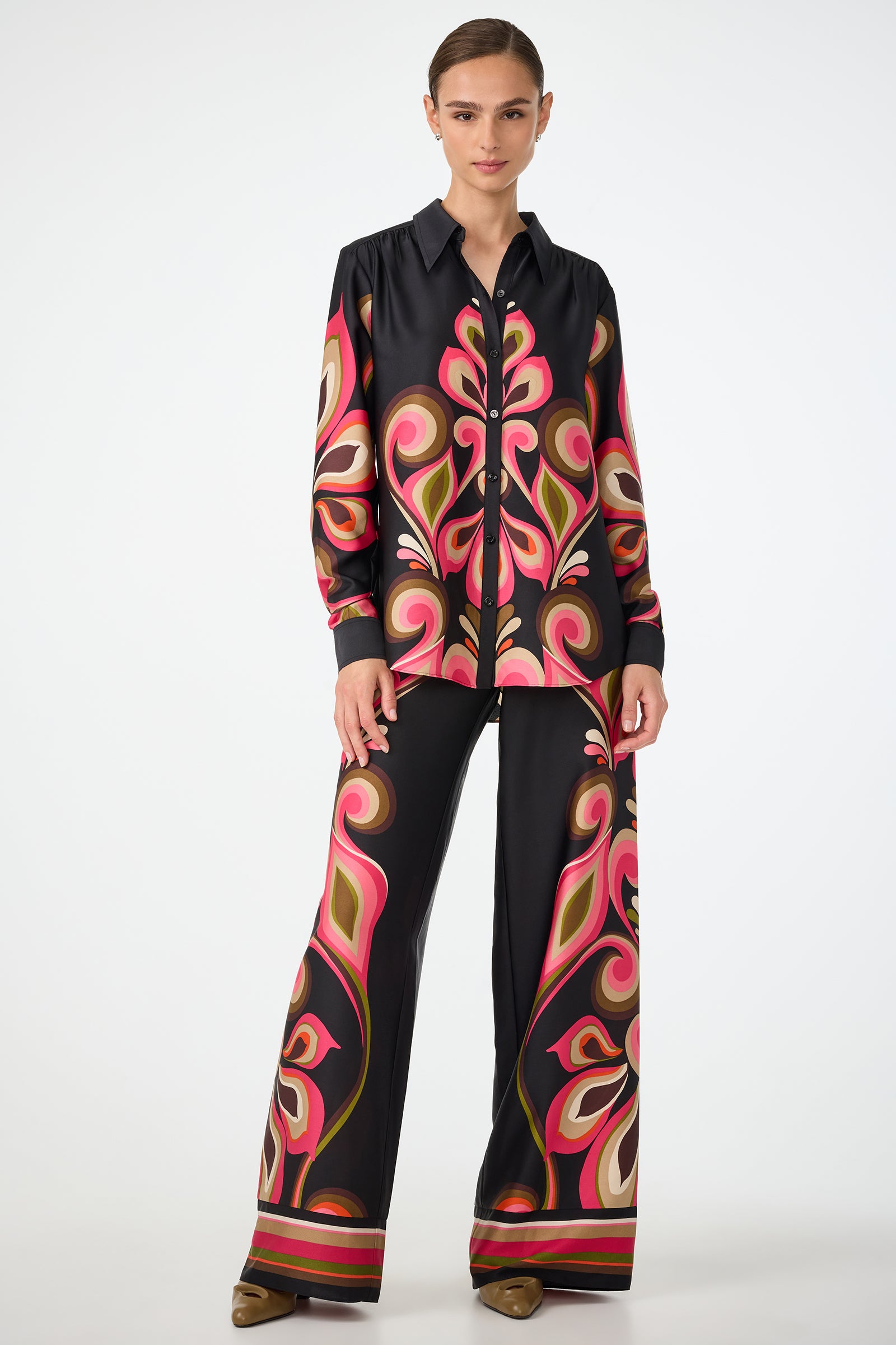 A woman wearing the Cassavetes Border Shirt - Sanctuary poses against a white background, paired with wide-leg pants featuring bold paisley prints in pink, orange, and beige. She has her hair tied back and wears brown shoes.