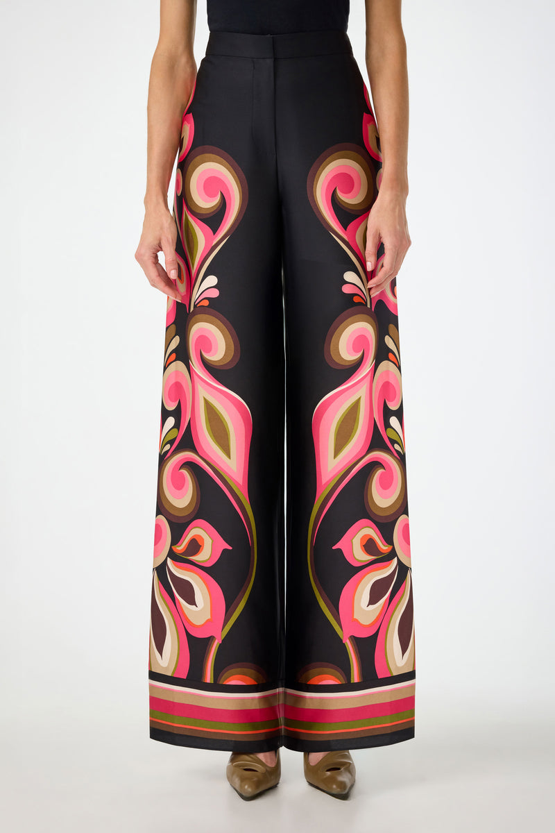 Someone wears the Verity Border Pants in Sanctuary—a high-waisted, wide-leg style featuring a bold paisley pattern in pink, orange, green, and cream—standing against a plain white background.