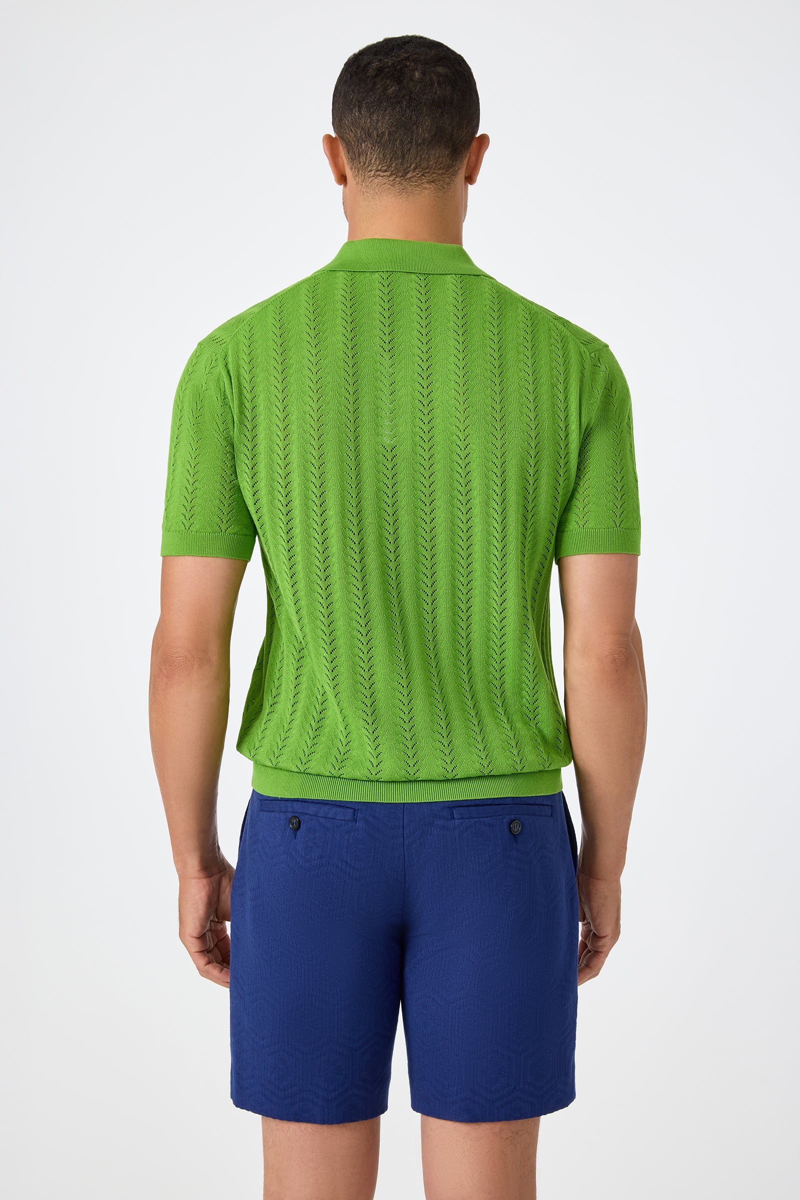 A man faces away from the camera, wearing the Cole Short-Sleeve Polo in bright green with a textured pattern and royal blue shorts against a plain white background.