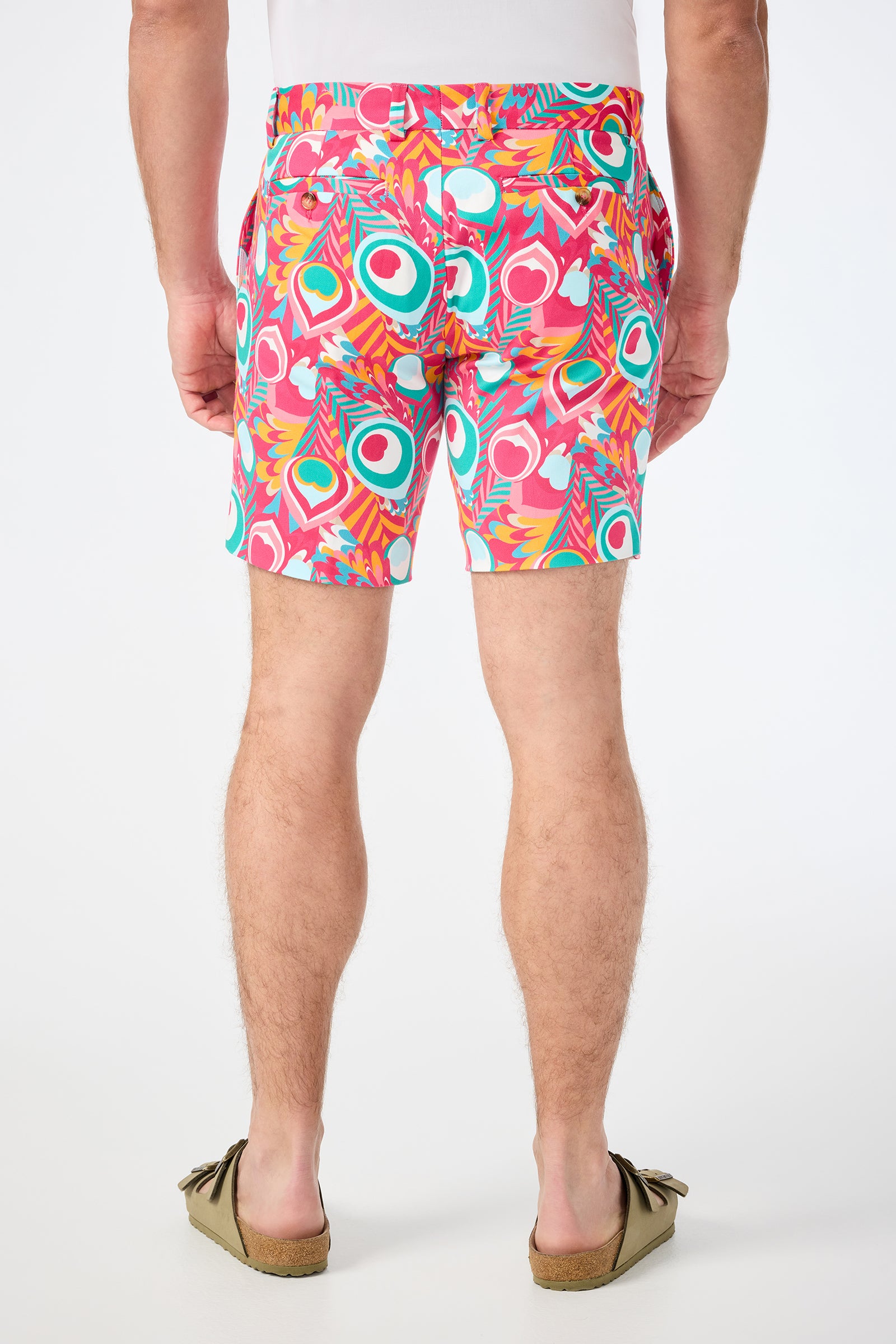 A person is seen from behind wearing the Lawrence Short - Dramont Herringbone, which features a colorful, abstract pattern with pink, teal, and yellow shapes. They also have on brown slip-on shoes.