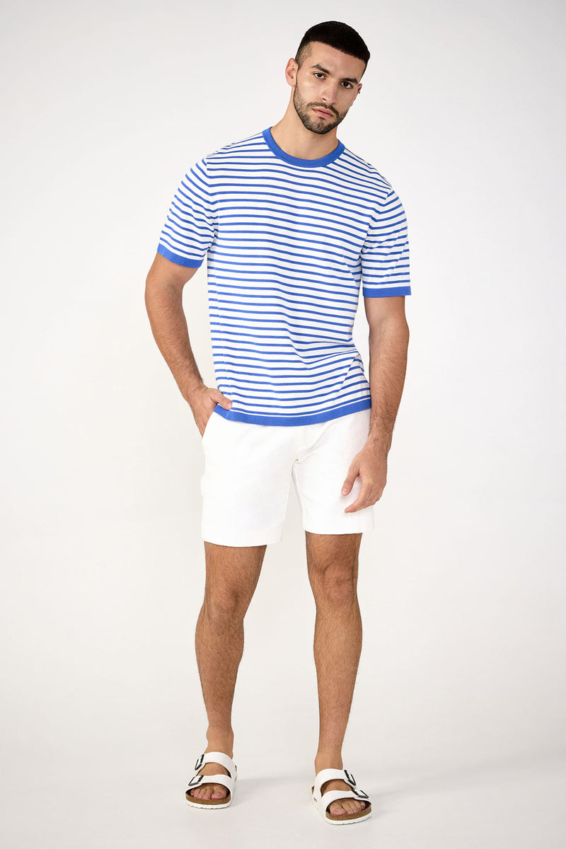 A man with short hair and a trimmed beard poses against a plain background, looking at the camera. He wears the Giovanni Stripe Short-Sleeve Pullover with white shorts and sandals, one hand in his pocket.