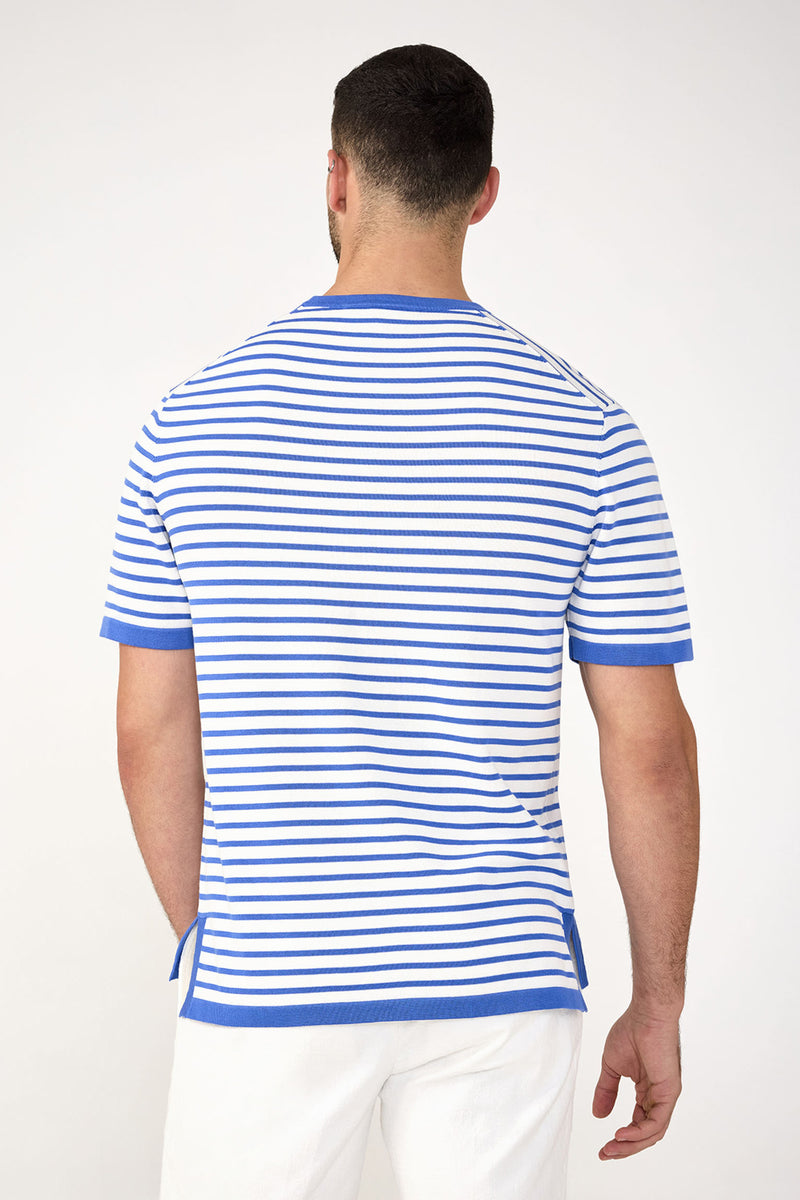 A man faces away from the camera, wearing the Giovanni Stripe Short-Sleeve Pullover—white with blue horizontal stripes and trim—paired with white pants, against a plain light background.