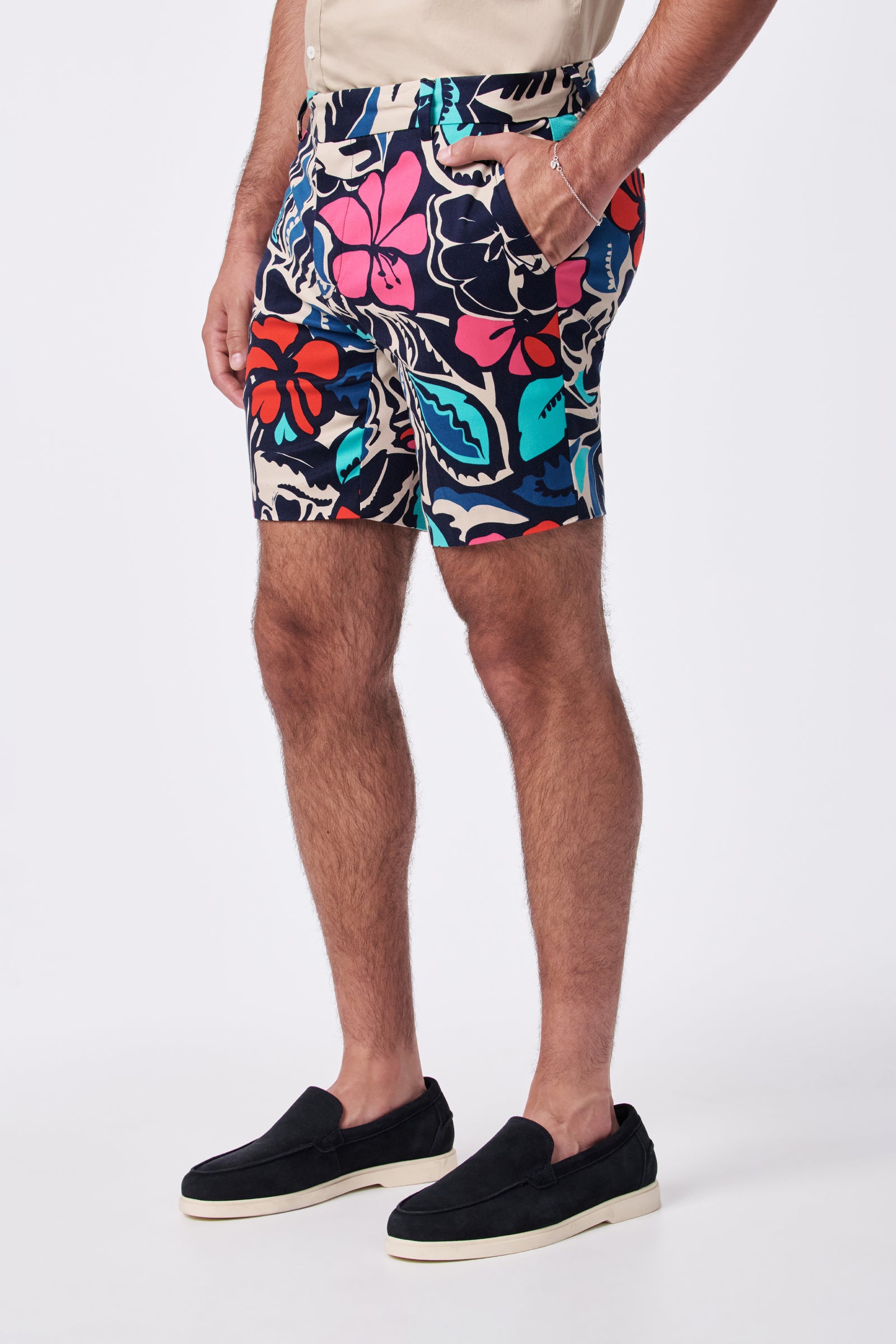 A person models the Lawrence Short, featuring a colorful floral print, paired with a beige tucked-in shirt and black slip-on shoes. Only the lower body is visible against a plain white background, with hands in pockets.