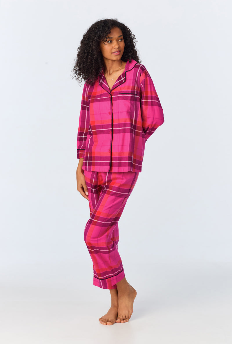 A woman stands barefoot against a light background wearing the Aurora Plaid Womens 3/4-Sleeve Cropped Pant Flannel PJ Set, looking off to the side.