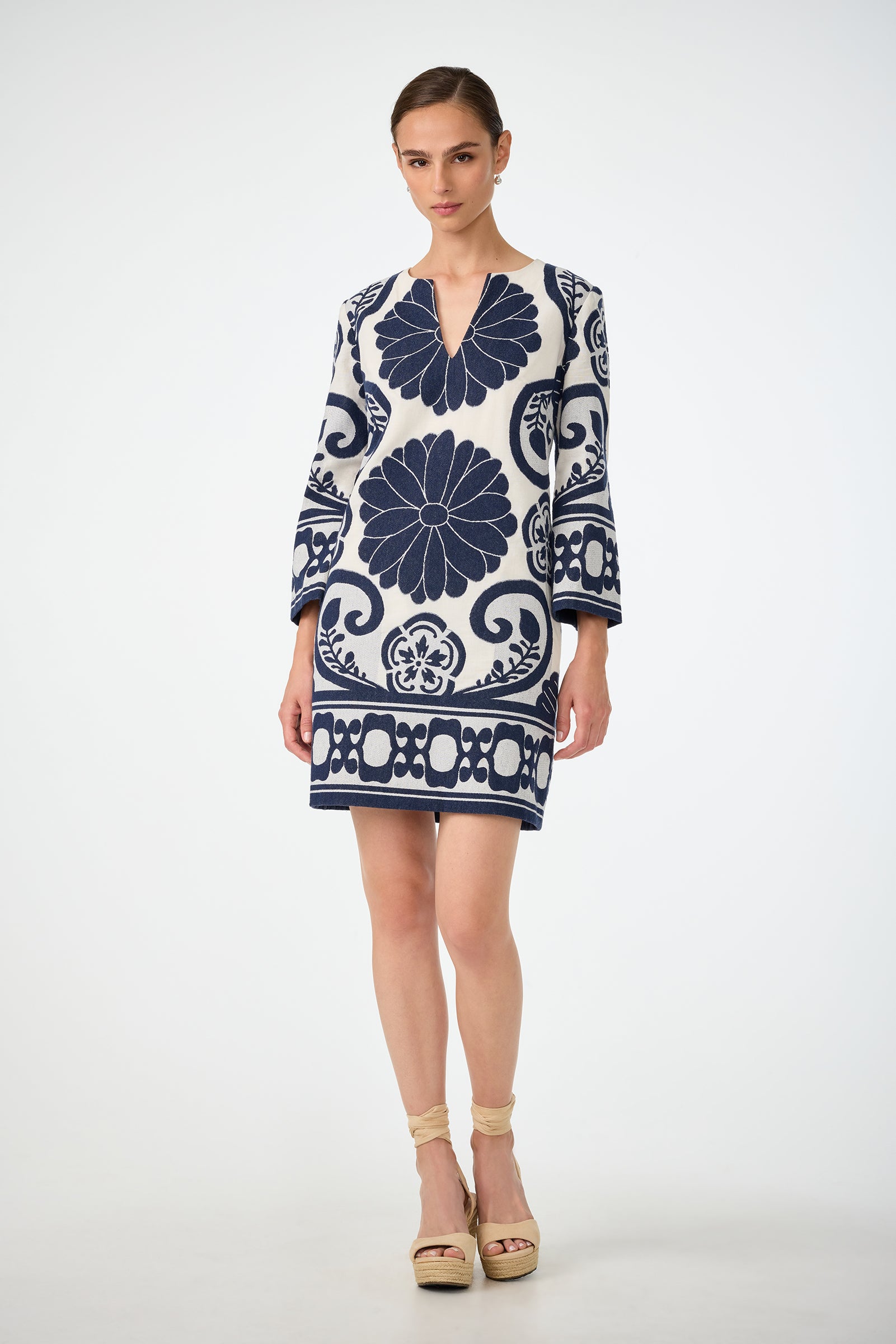 A woman stands against a white background wearing the Amy 3/4 Sleeve Dress in Fuyuko Fil Coupe, featuring bold navy blue floral and geometric patterns. Her hair is tied back, and she pairs the dress with beige platform sandals.