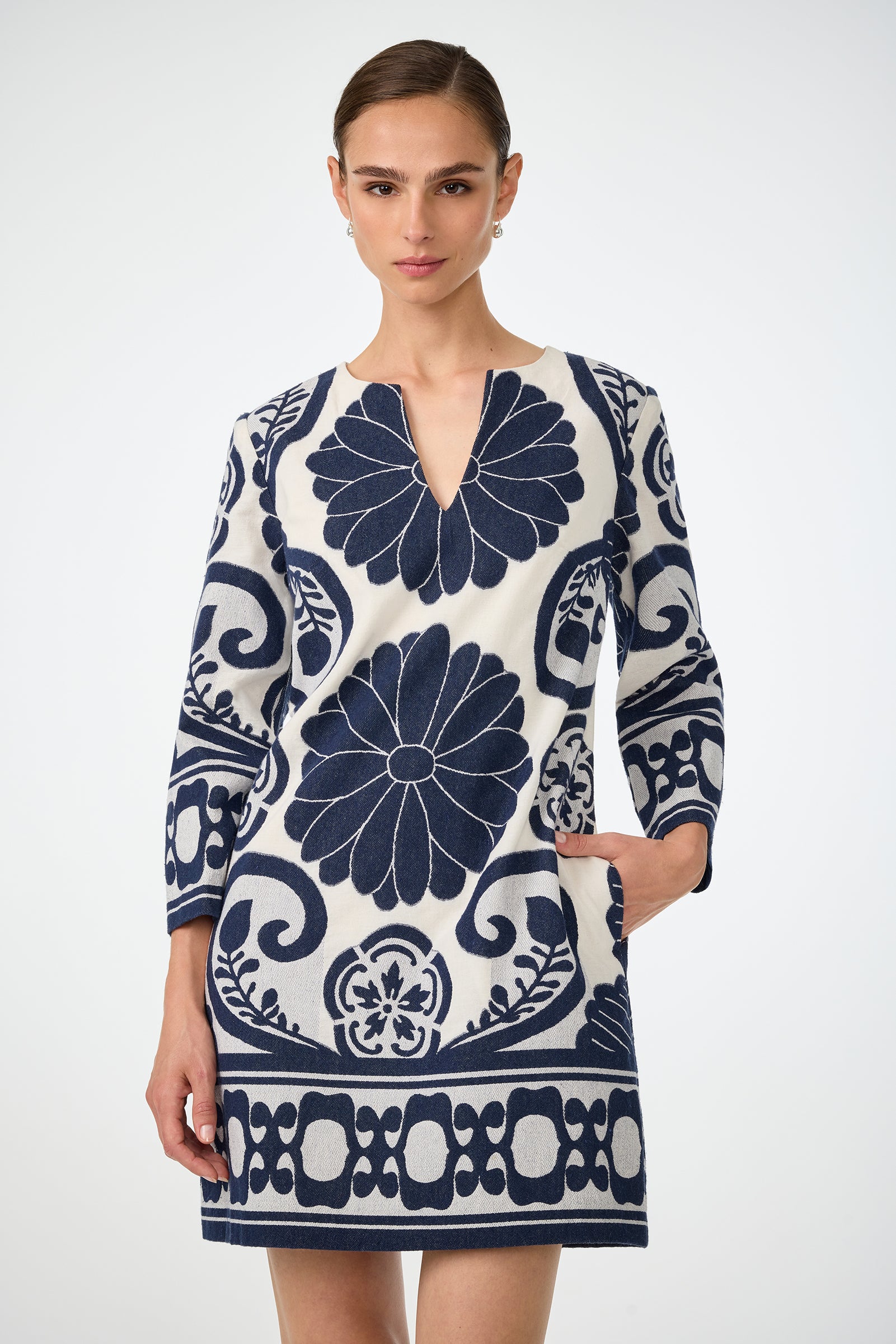 A woman wears the Amy 3/4 Sleeve Dress - Fuyuko Fil Coupe, a white dress featuring bold navy blue floral and geometric patterns, standing against a plain white background.