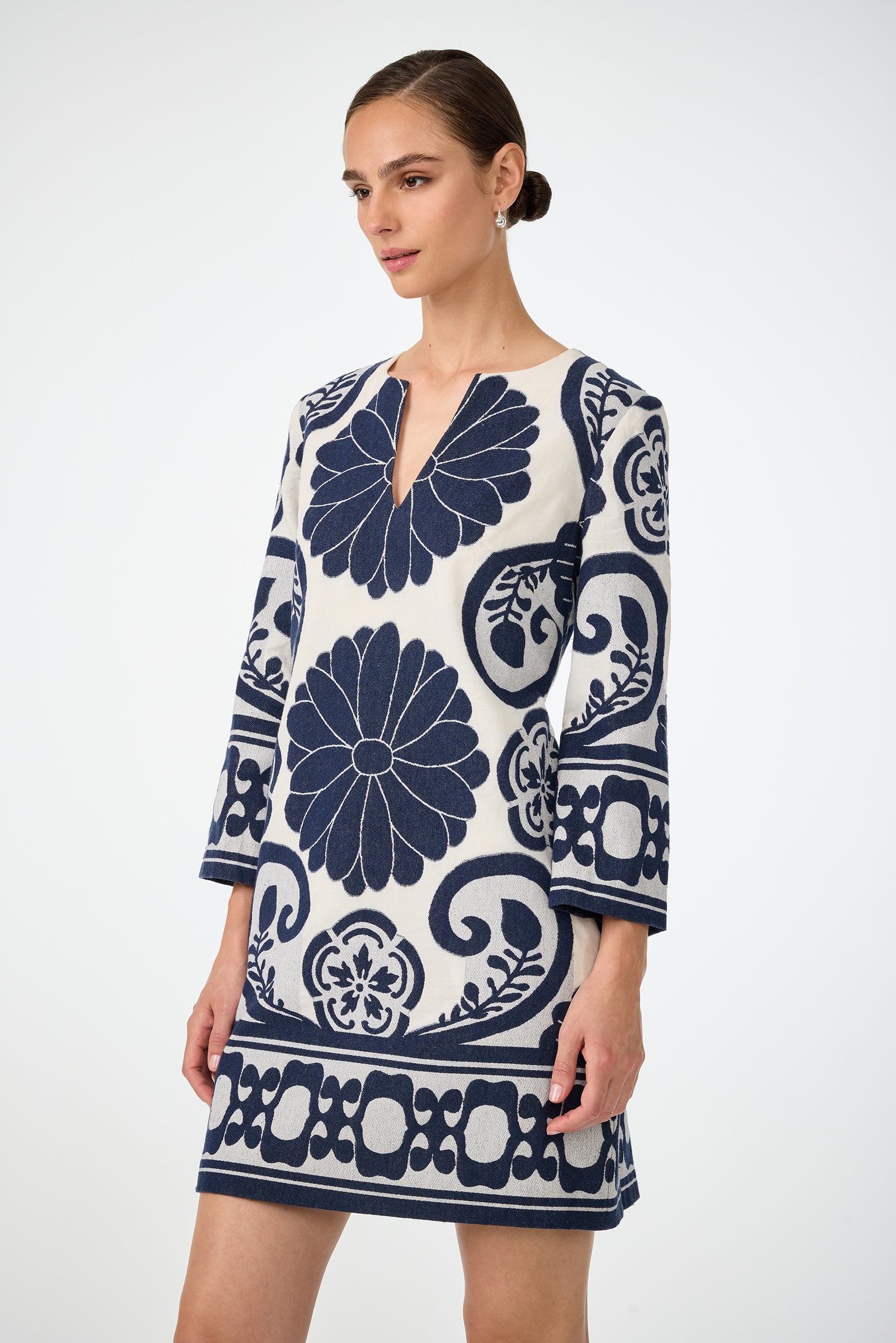 Woman wearing the Amy 3/4 Sleeve Dress - Fuyuko Fil Coupe, a white dress with bold navy blue floral and geometric patterns, three-quarter sleeves, and a notched neckline, standing against a plain light background.