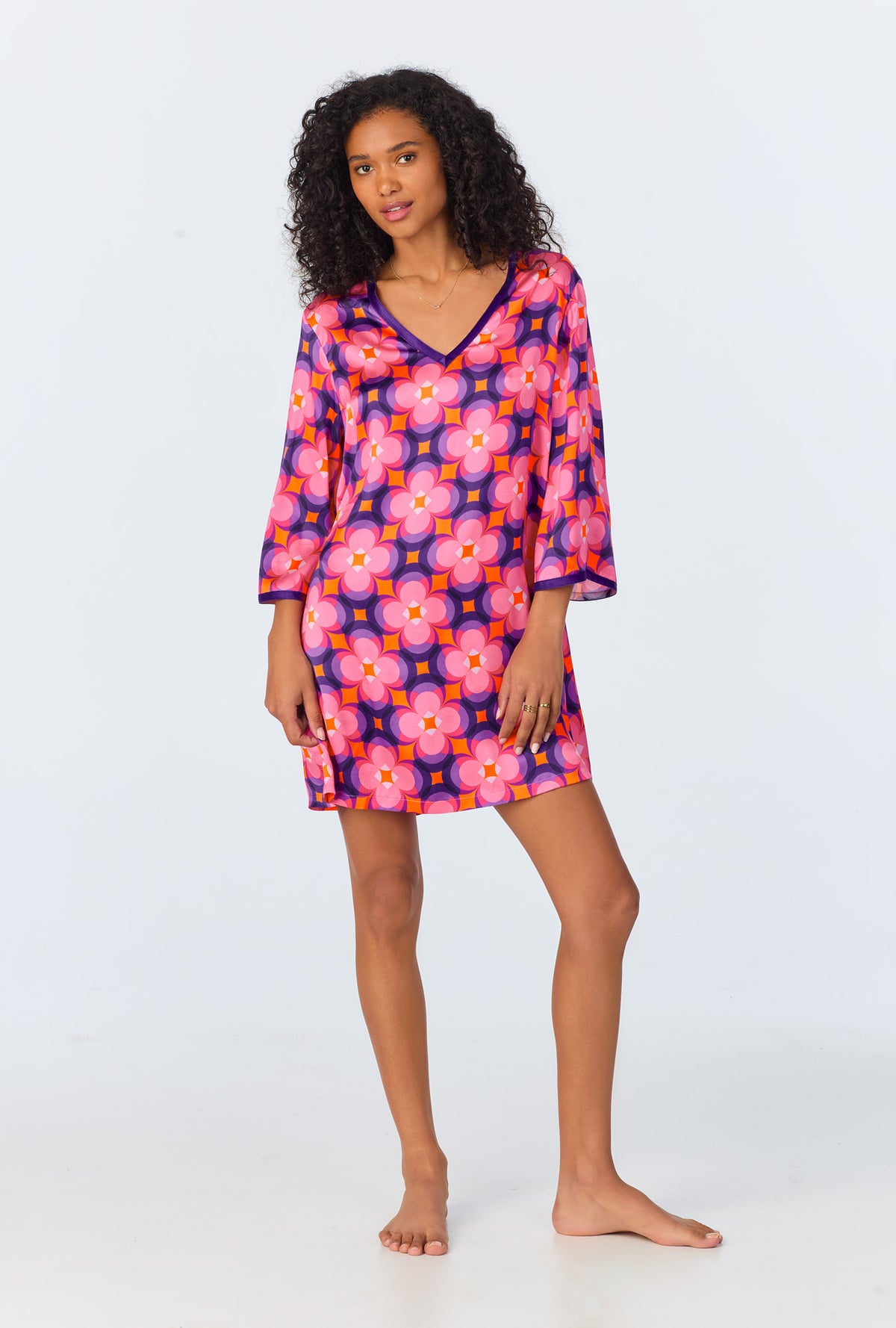 A woman stands barefoot in the Space Cat Womens 3/4-Length Sleeve Silk Caftan in multi, featuring a bold retro floral pattern, against a plain light background.