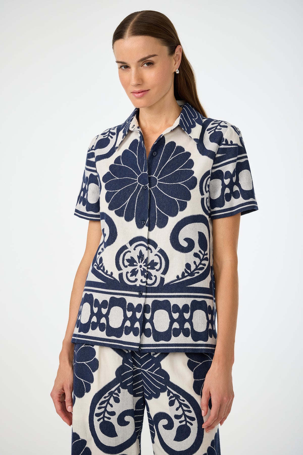 A woman with straight brown hair wears the Abba Top in Fuyuko Fil Coupe, featuring a bold navy and white floral and geometric pattern, against a plain light background.