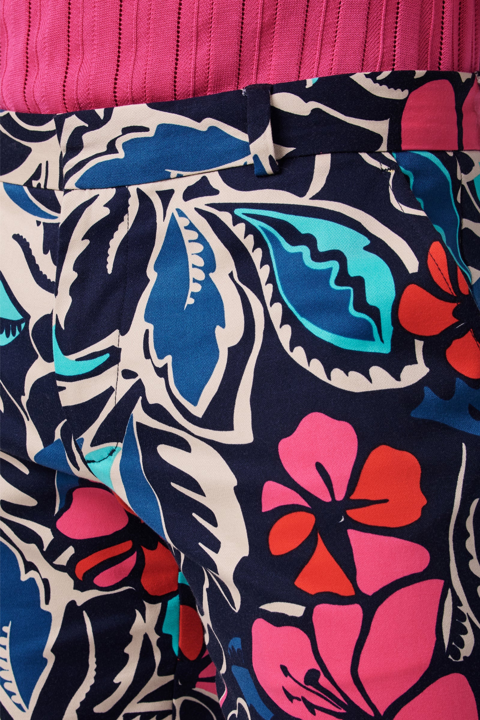 Close-up of a person wearing the Clyde Slim Trouser, featuring a bold, colorful floral pattern in blue, pink, red, teal, and white, paired with a pink ribbed top.