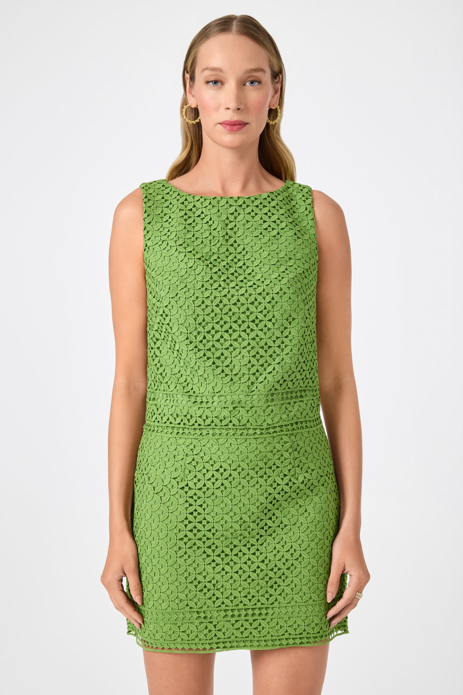 A woman with long blonde hair models the Cayley 2 Top in Lumi Lace, a sleeveless green crochet design, standing against a plain white background.