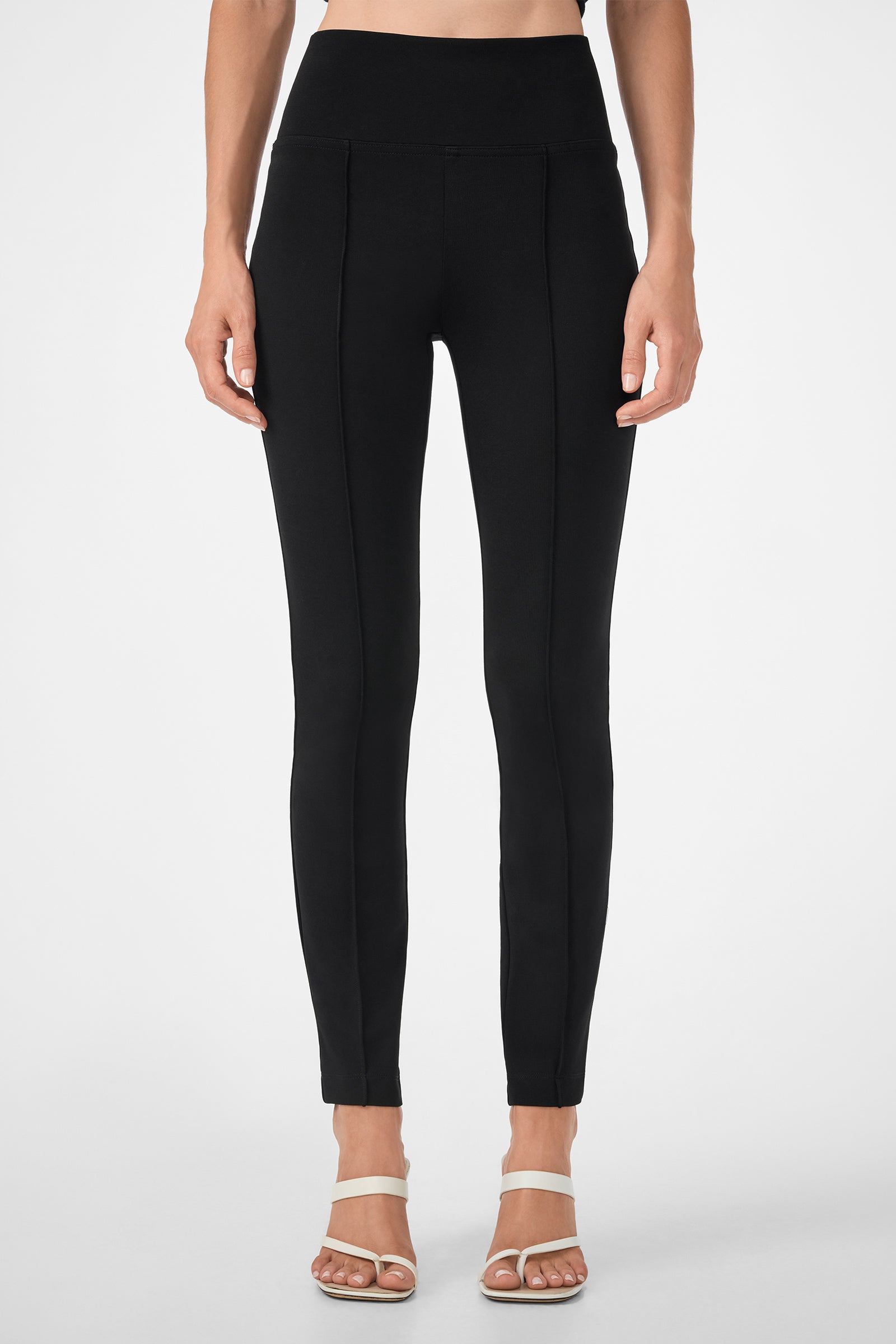 A person wearing the Rose Pant—high-waisted, fitted black pants with front seam details—and white open-toe sandals, standing against a plain light background.