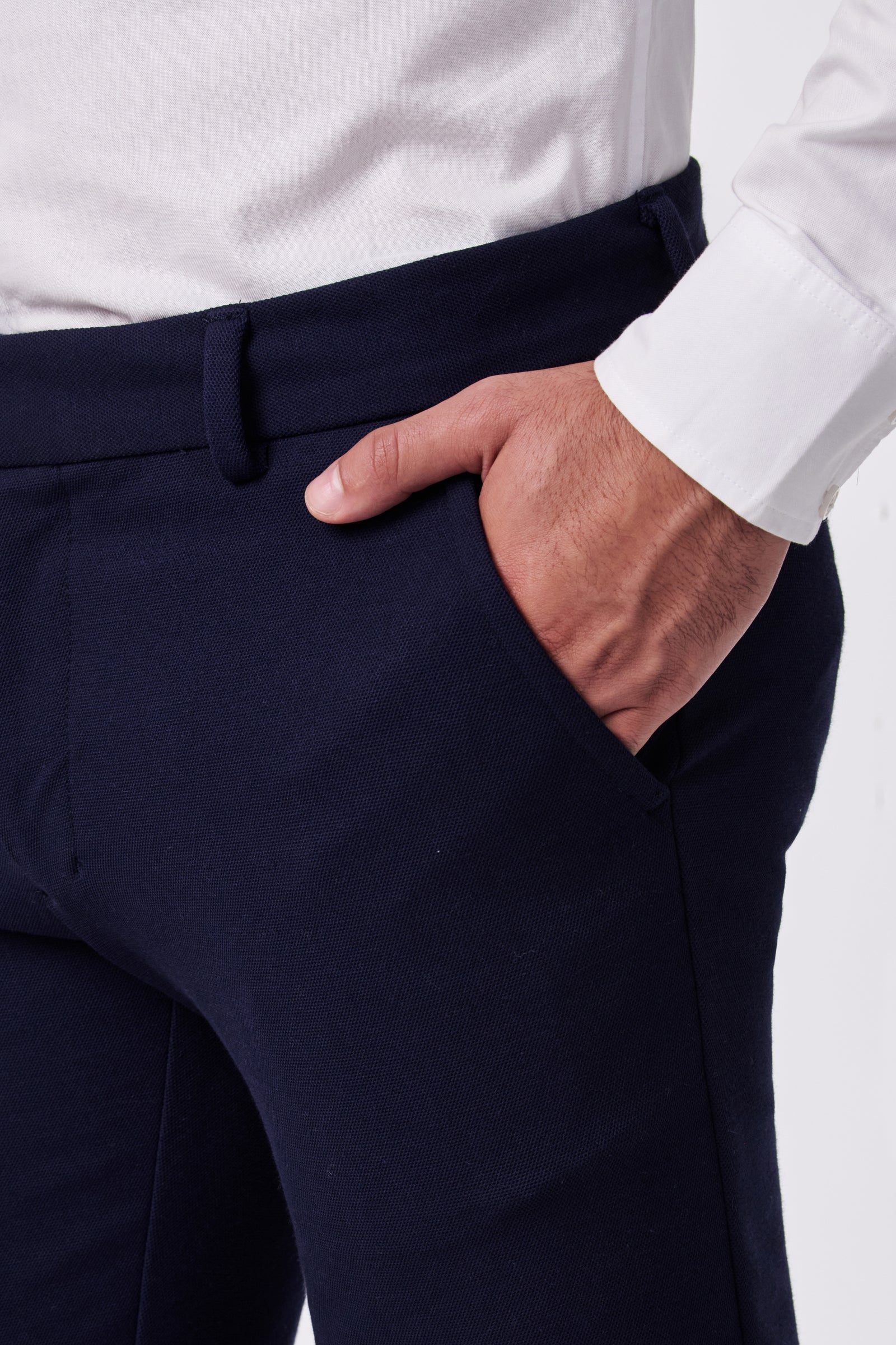 A person wearing Clyde Slim Trouser - Stretch Piqué stands with their right hand in their pocket. The image focuses on the midsection and hand.