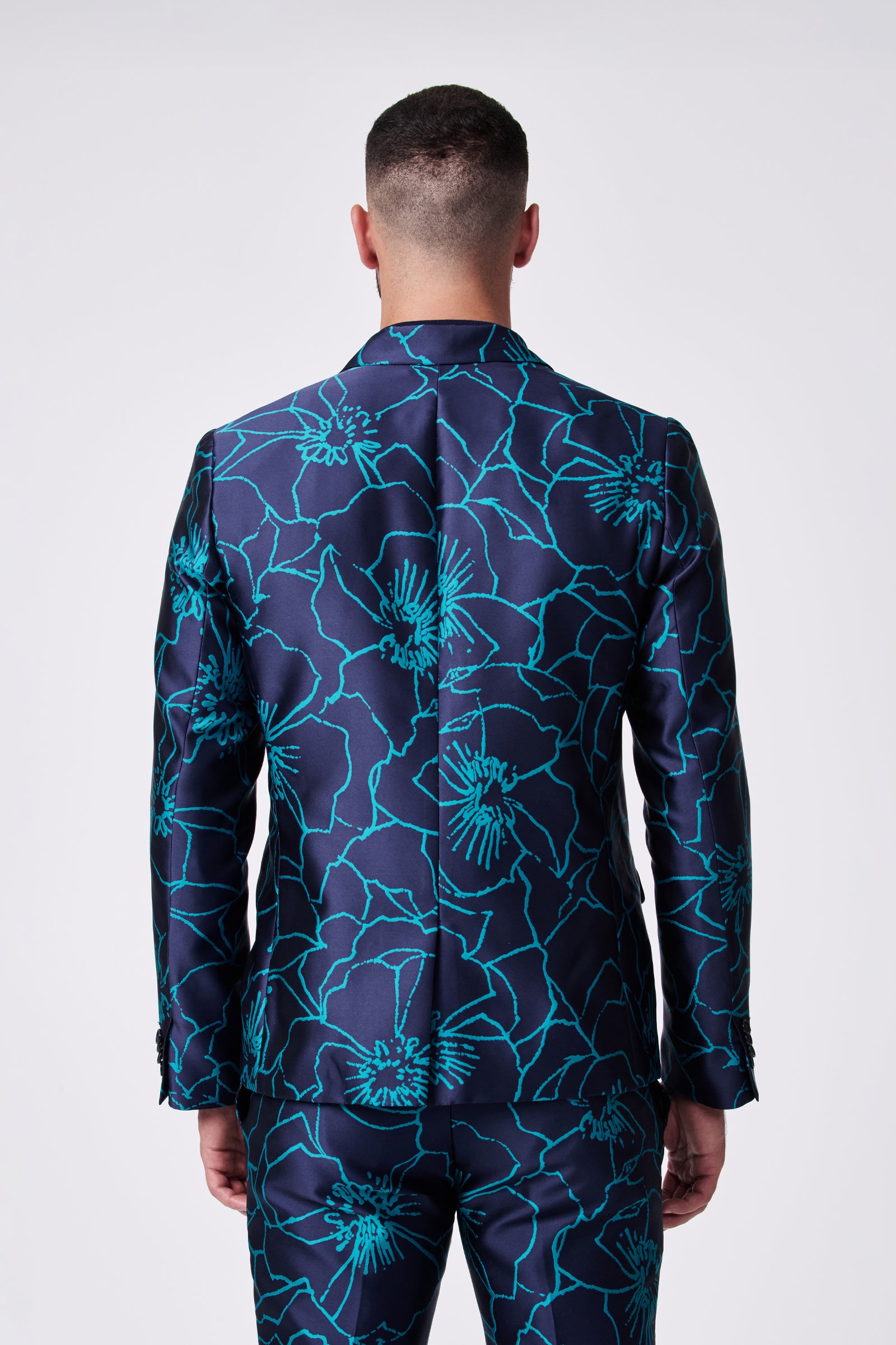 A man is seen from behind wearing the Thurston Blazer, a navy suit with a bold turquoise floral pattern. The plain, light background highlights the blazer's vibrant design.