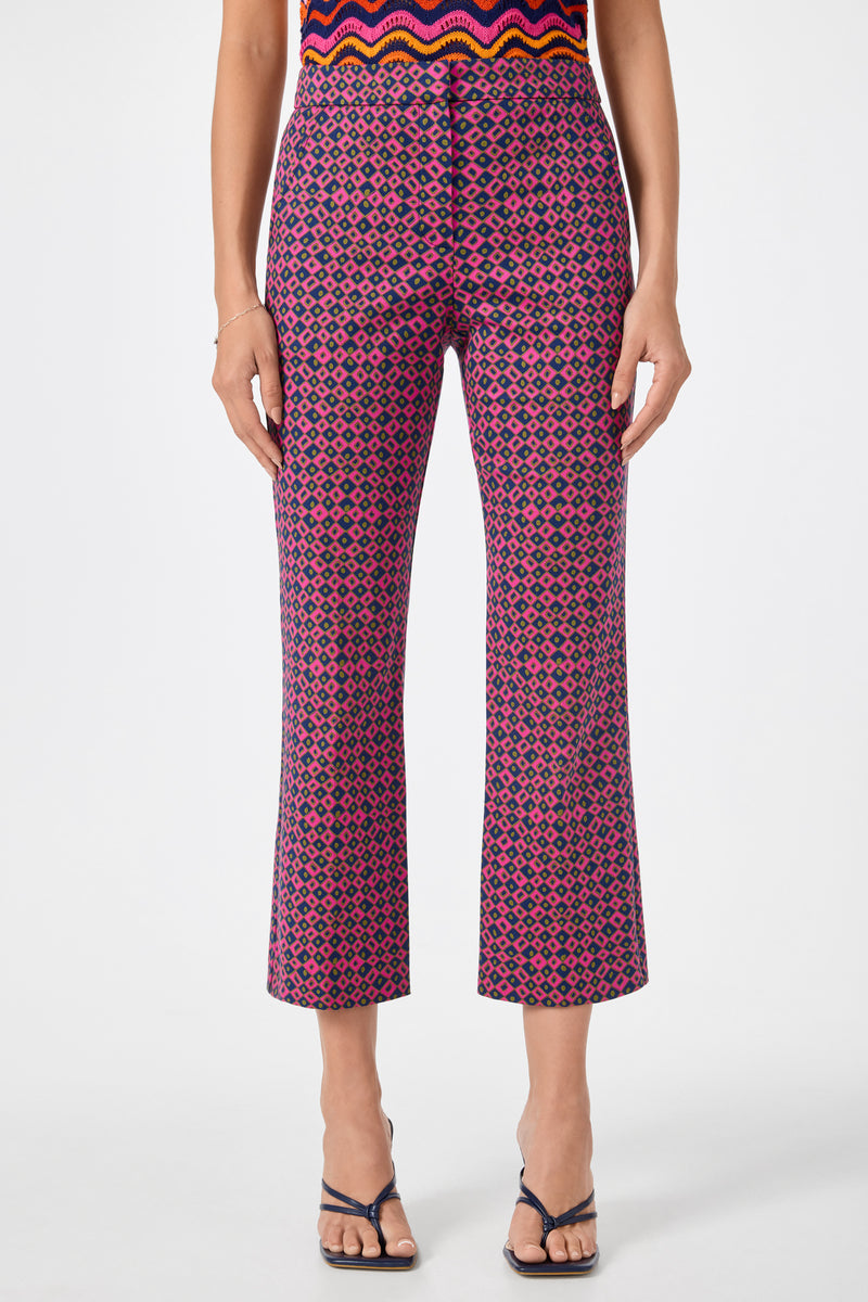 A person wearing the Lulu Cropped Pants - Himari Herringbone, featuring a high-waisted, geometric pink and navy pattern, paired with black strappy heeled sandals and a colorful top.