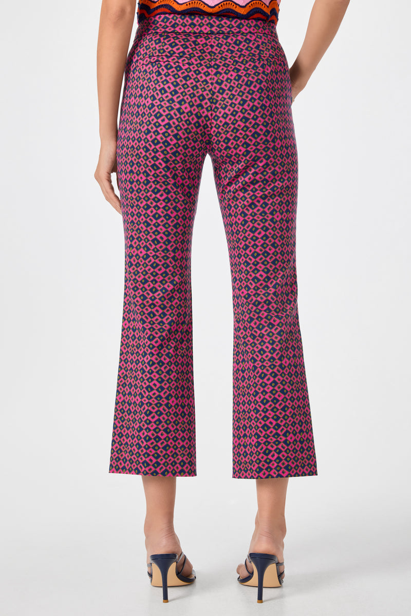 A woman faces away from the camera, wearing Lulu Cropped Pants - Himari Herringbone with a pink and black geometric pattern, black heeled sandals, and a partially visible orange patterned top.