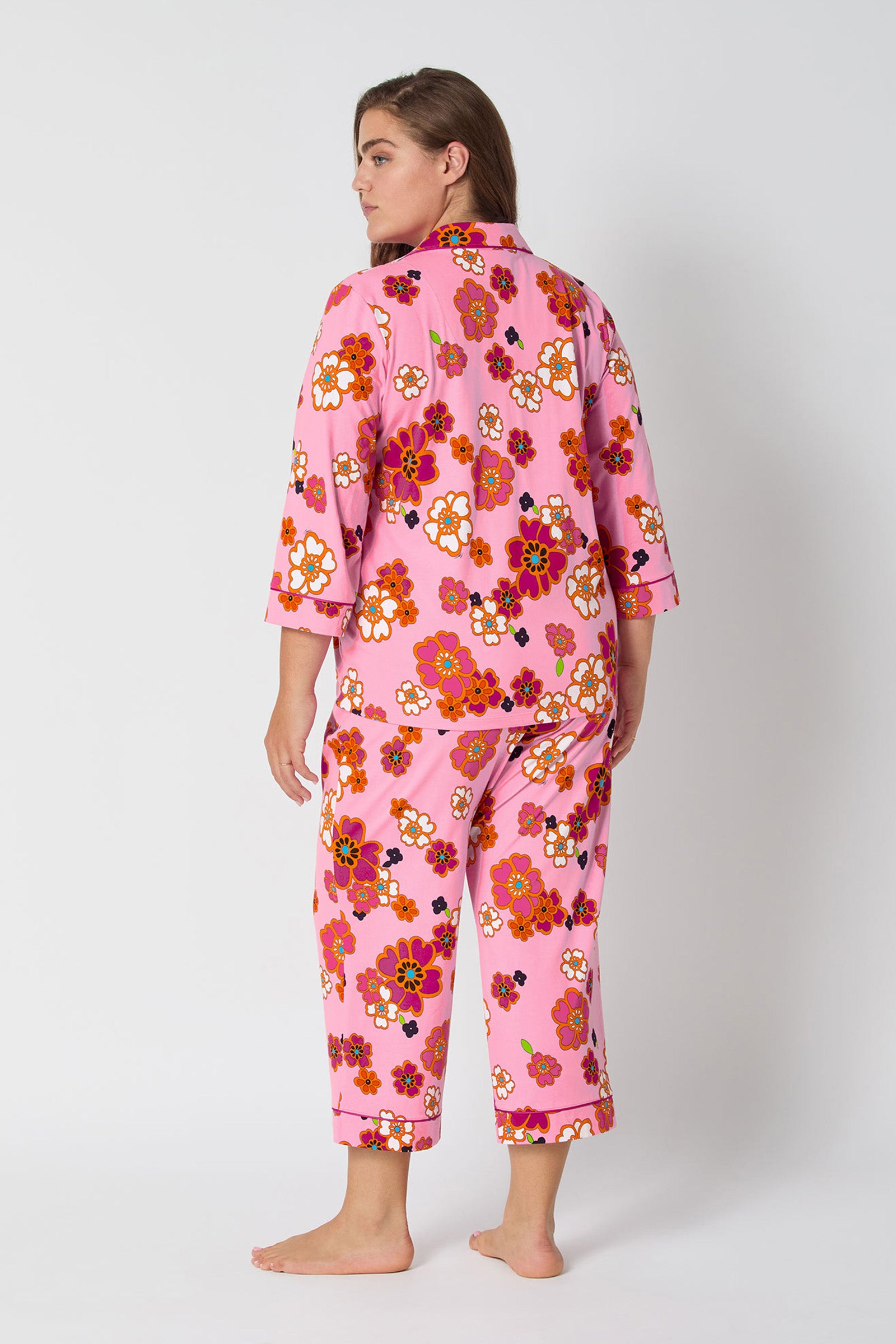 A woman faces away barefoot in the Resort Floral 3/4 Cropped Pj—pink pajamas with a bold floral print, three-quarter sleeves, and loose cropped pants—against a plain white background.
