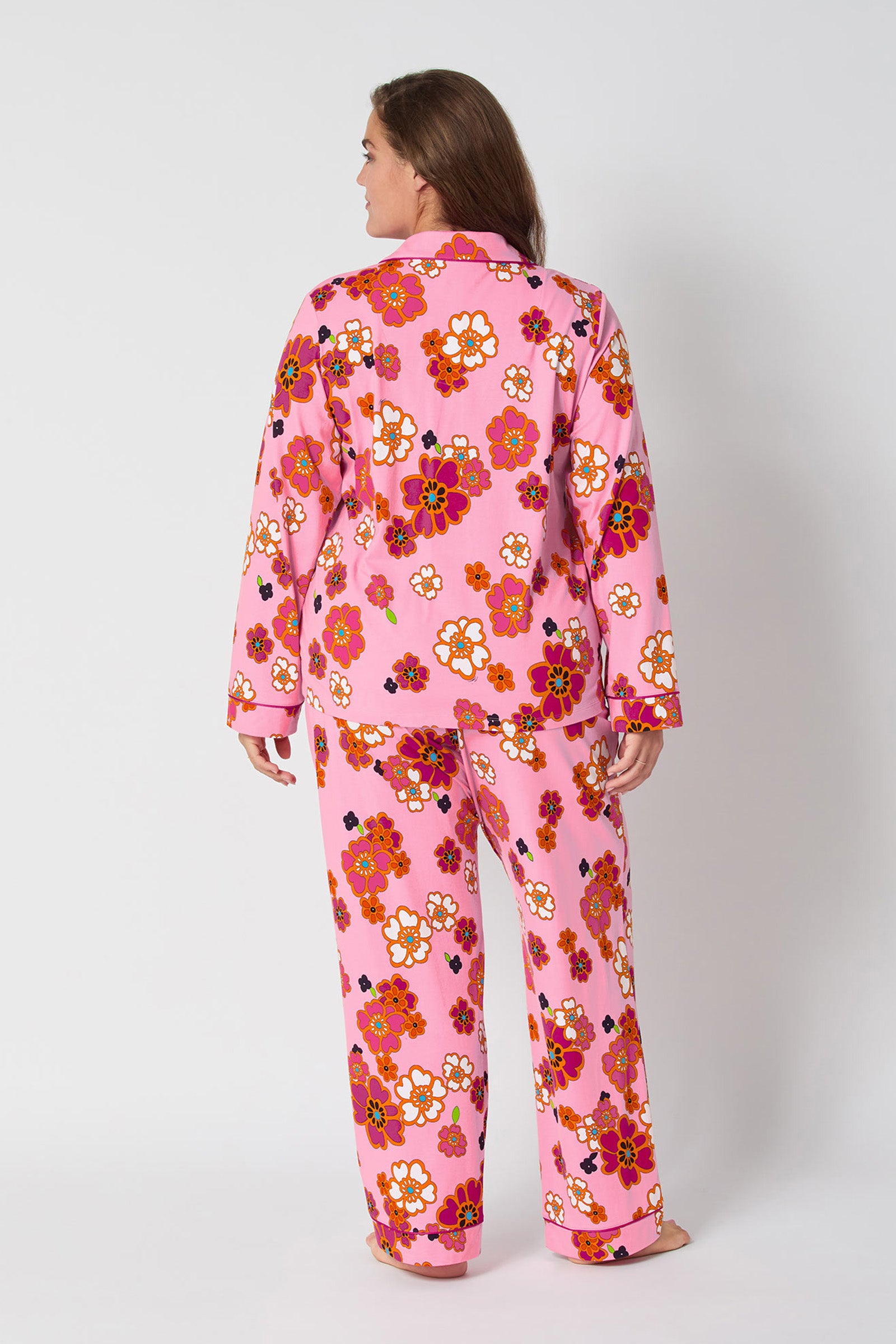 A person faces away in the Resort Floral L/S Classic Pj, featuring pink pajamas with a vibrant red, orange, and white floral pattern. The set includes a long-sleeve button-up top and matching pants against a plain white background.