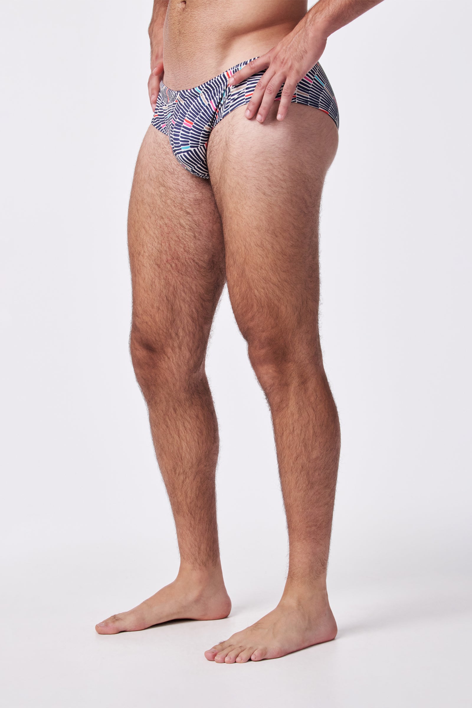A man models the Bondi Swim Trunk, featuring a blue, red, and white geometric pattern. The image captures his lower body and part of his torso from a side angle on a white background.