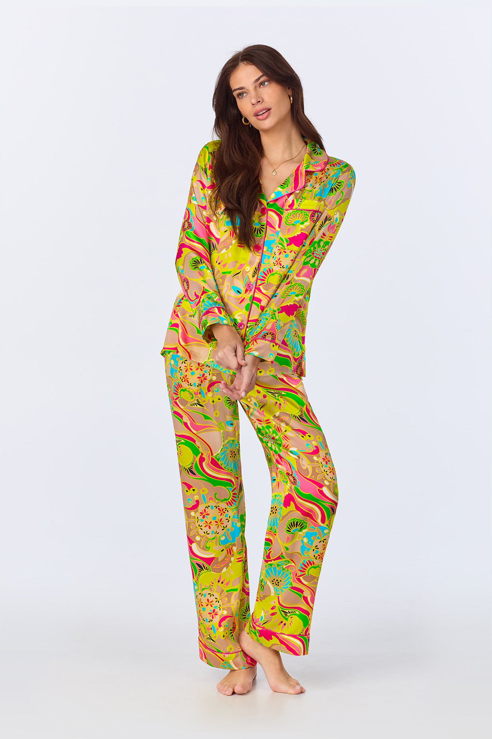 A woman with long brown hair stands barefoot against a plain background, wearing the TT LS Pant PJ Set - Heritage Silk in a vibrant multi-colored pattern.