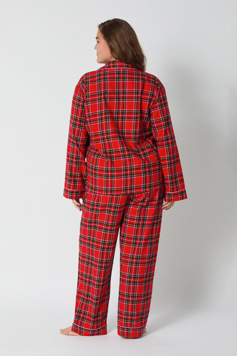 A person stands barefoot facing away against a plain light background, wearing the Christmas Plaid L/S Classic Pj set featuring red, black, green, and white plaid with long sleeves and long pants.