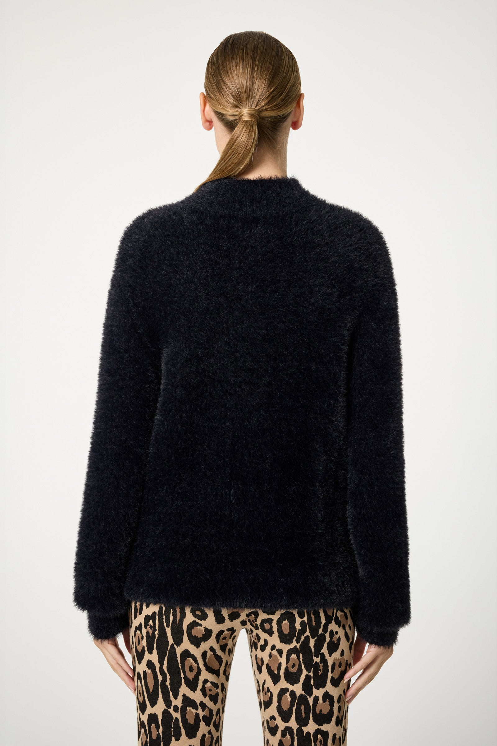 A person with straight brown hair in a low ponytail is seen from behind, wearing the Bazaar Mock Neck Sweater and leopard print pants against a plain white background.